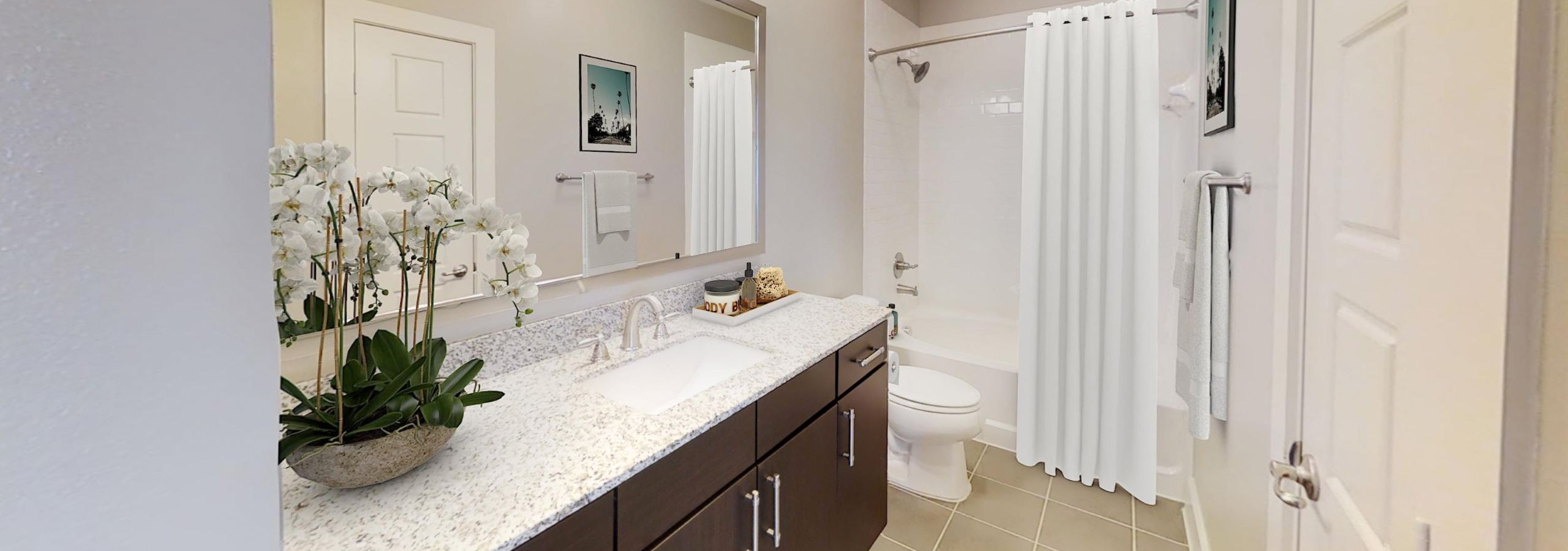 AMLI at the Ballpark bedroom with a bed with gray and white linens and a bench at the foot and a window and three pieces of art on the walls