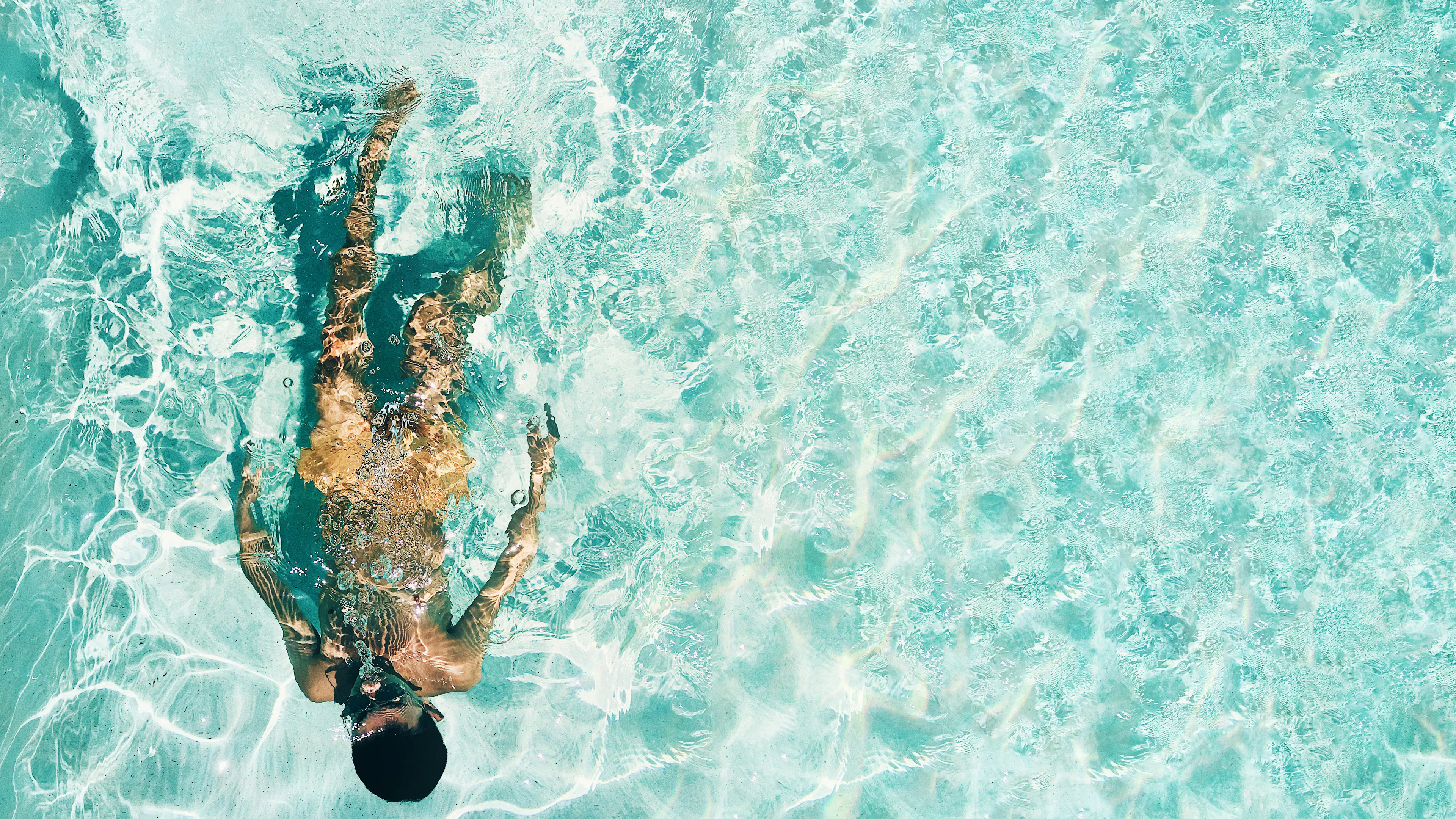 A person swimming in a shallow sandy shoal with the sunlight reflecting in waves over the sand