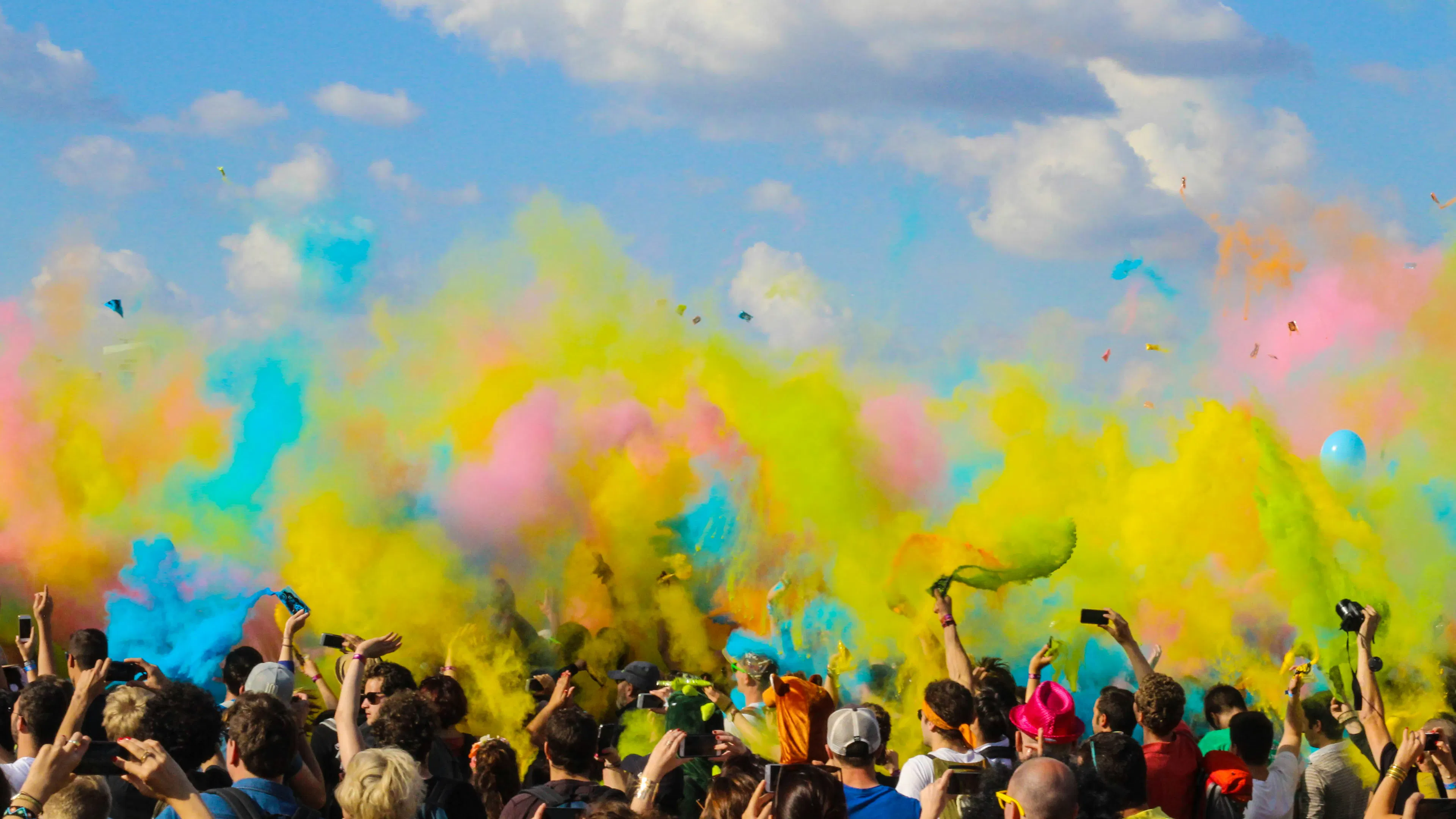 A crowd of people facing away from the camera and a thick cloud of colorful dye powder just thrown in the air above them