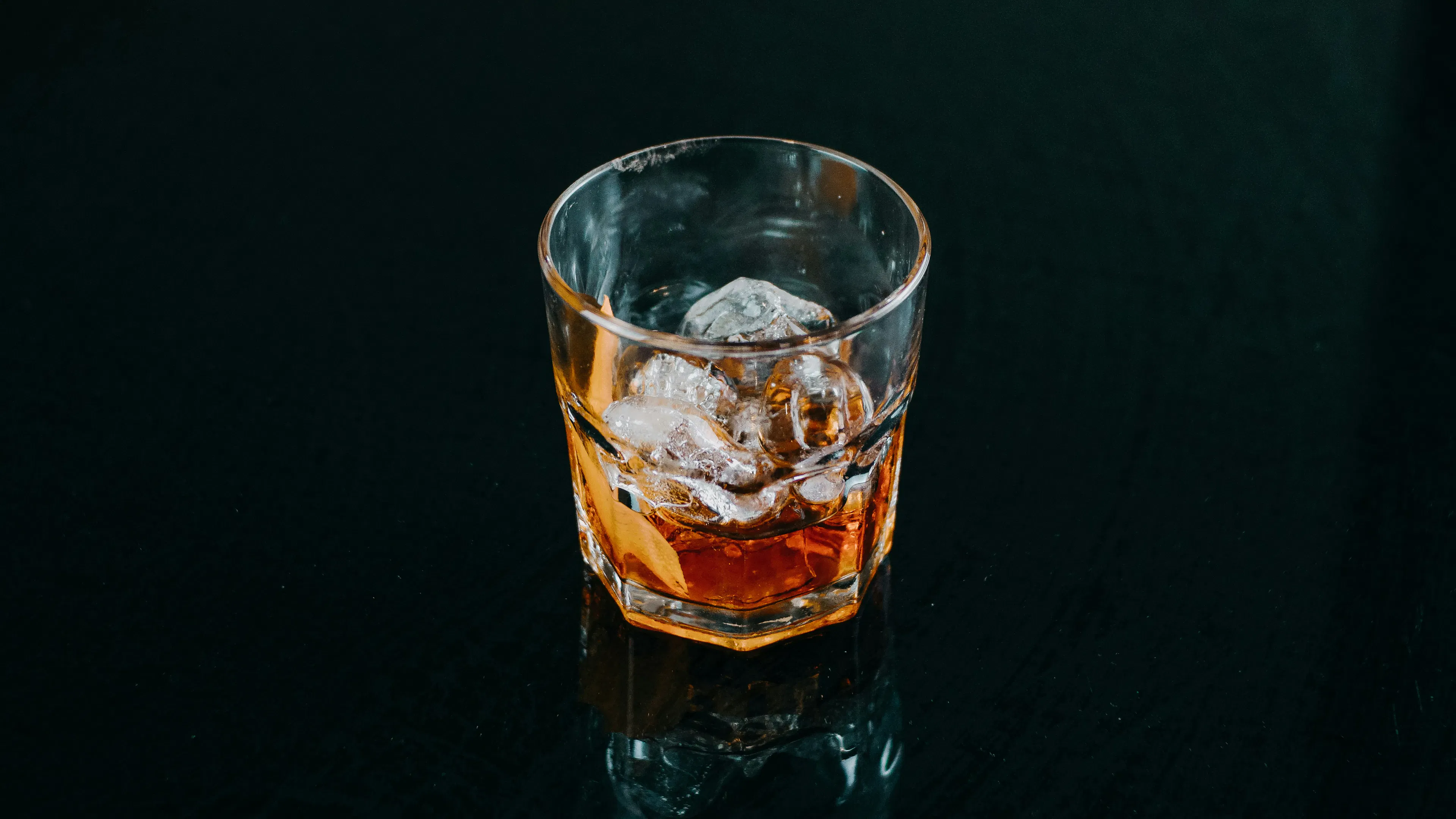 A single glass of liquor against a dark black ackground