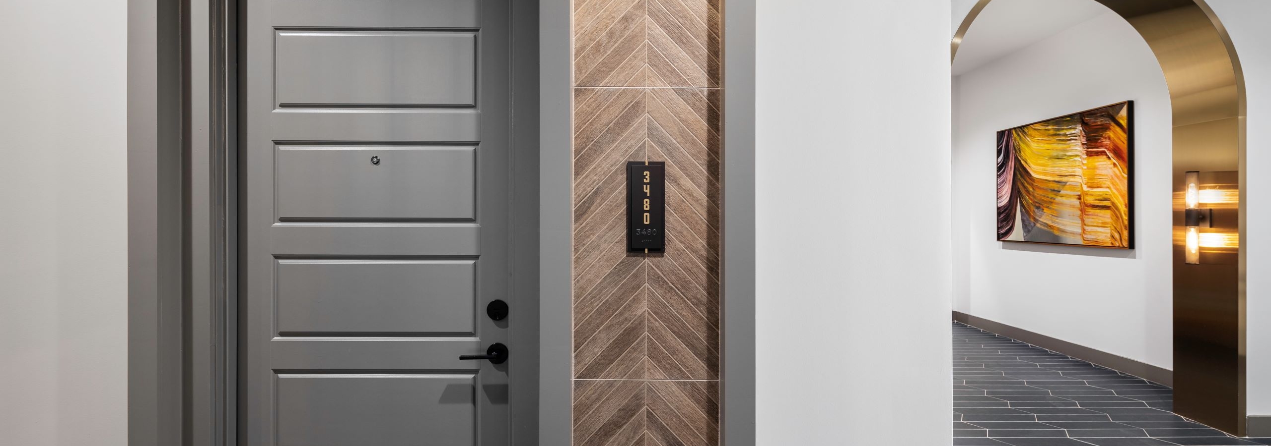 Gray six-panel interior hall door with wood herringbone panel and black number plaque with gold archway at AMLI Flatiron