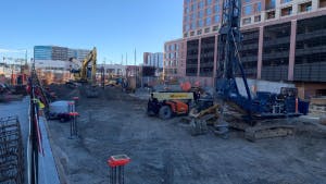 Construction site and AMLI Golden Triangle with a large crane and trucks sitting on dirt under a blue sky with scattered clouds