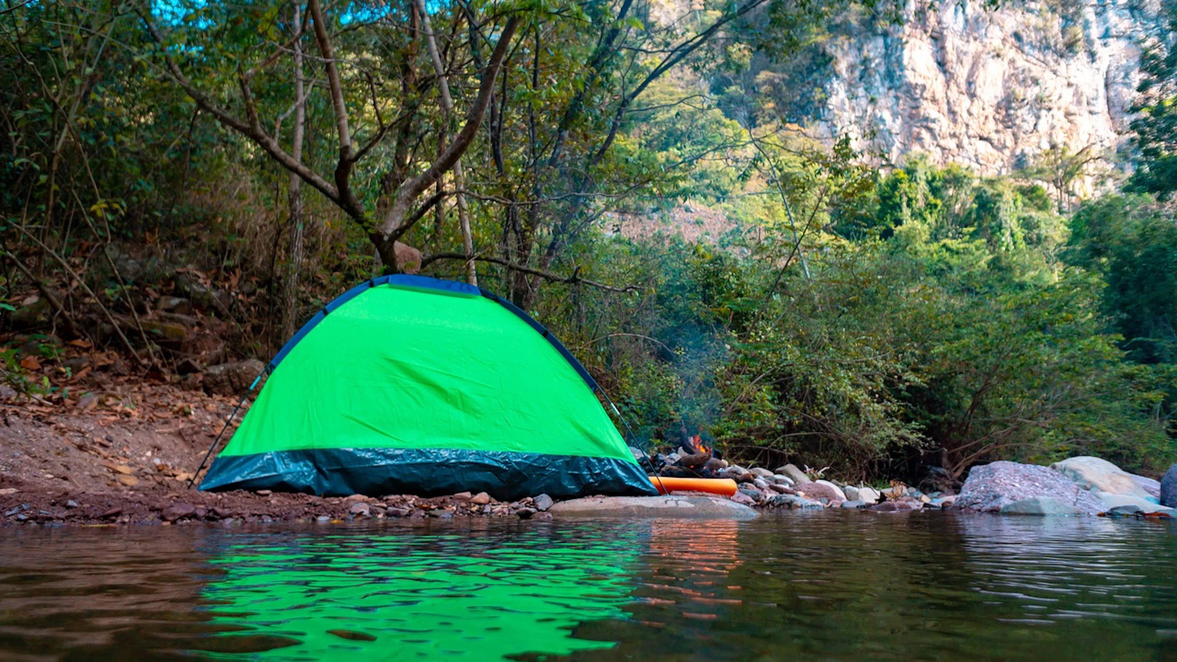 green tent in the woods by a lake with mountains in the background