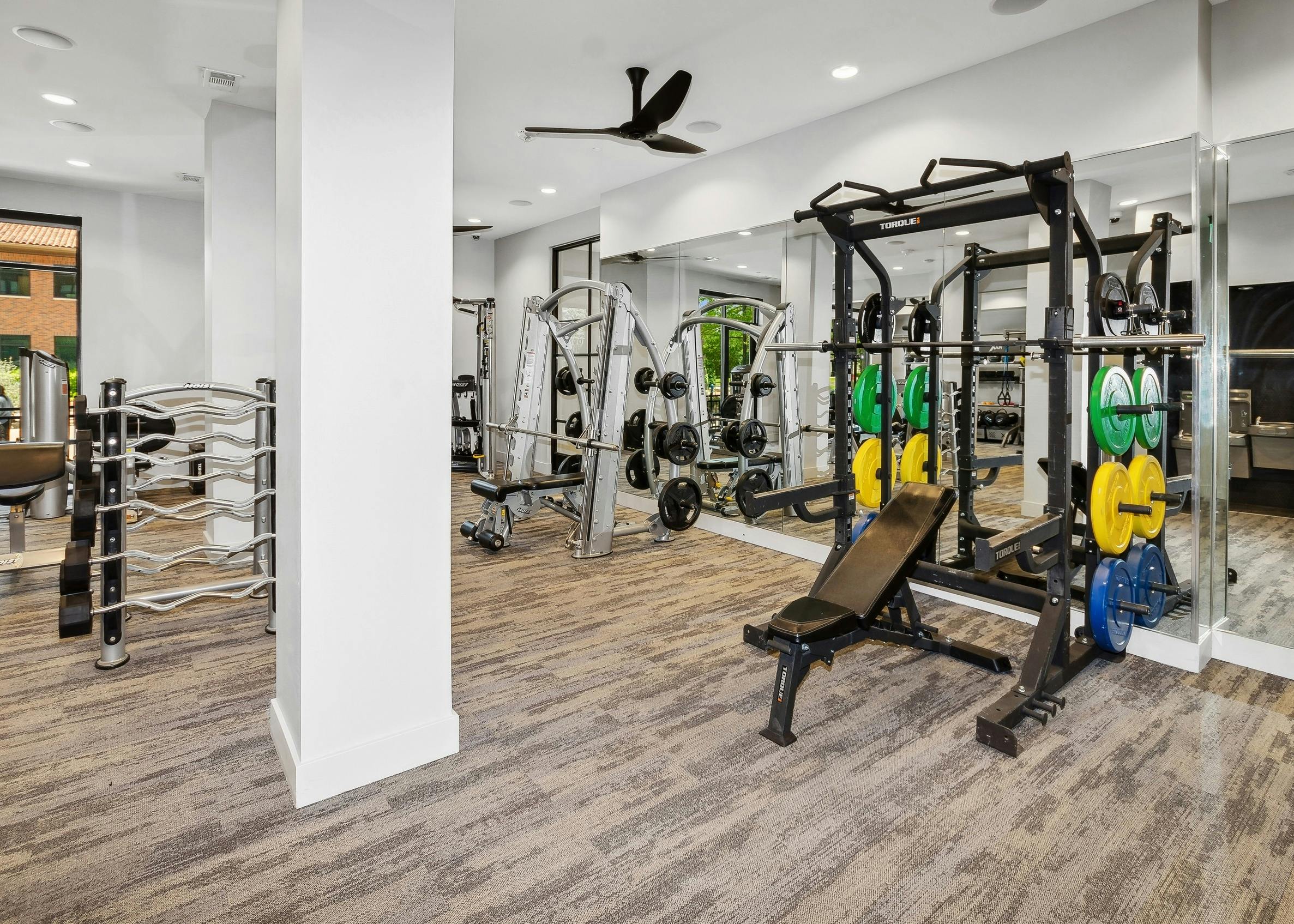 Carpeted gym at AMLI Addison with a mirrored wall with strength equipment including two large weight benches and weights
