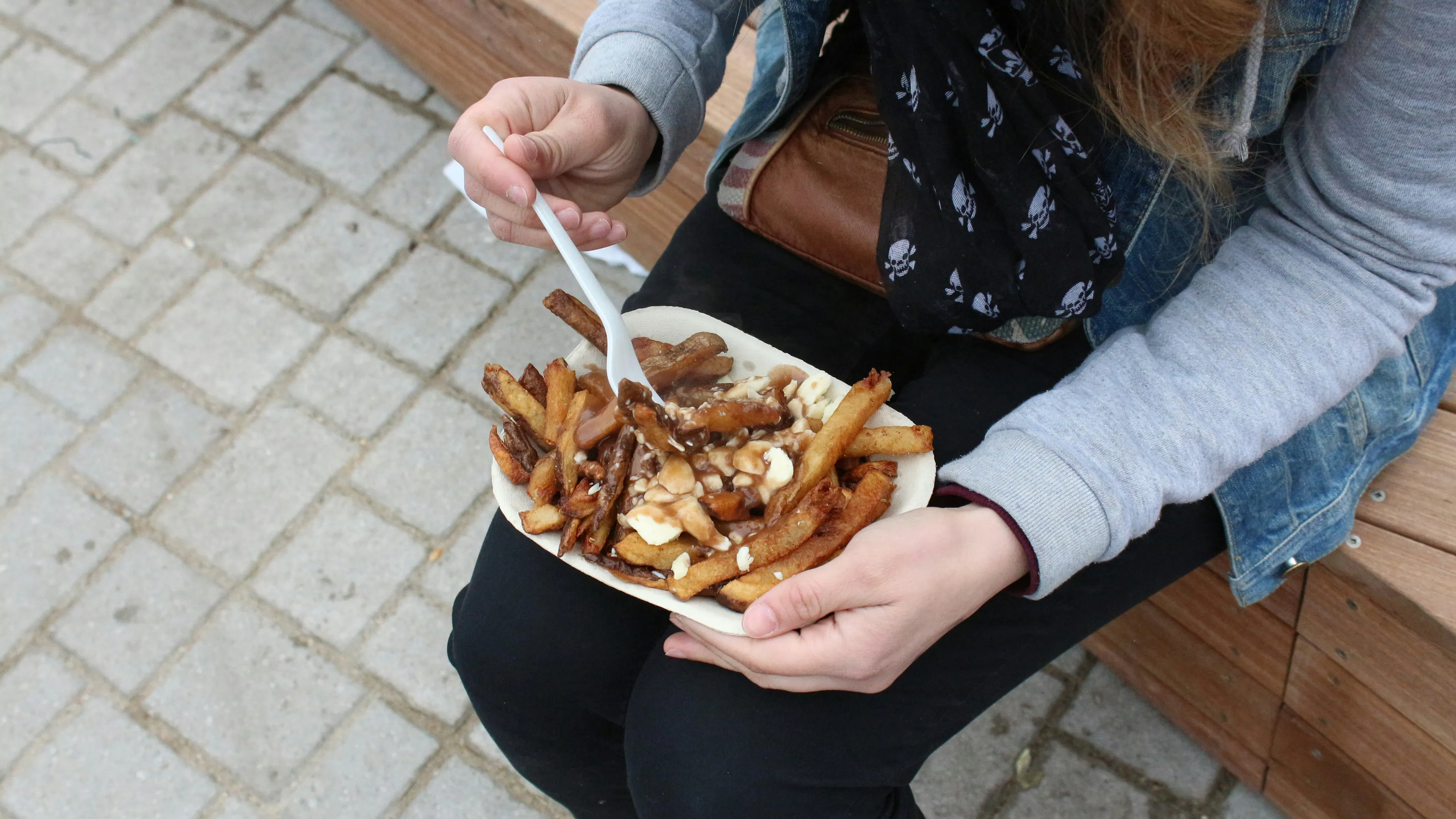 A woman holding a plate of poutine and a fork on her lap