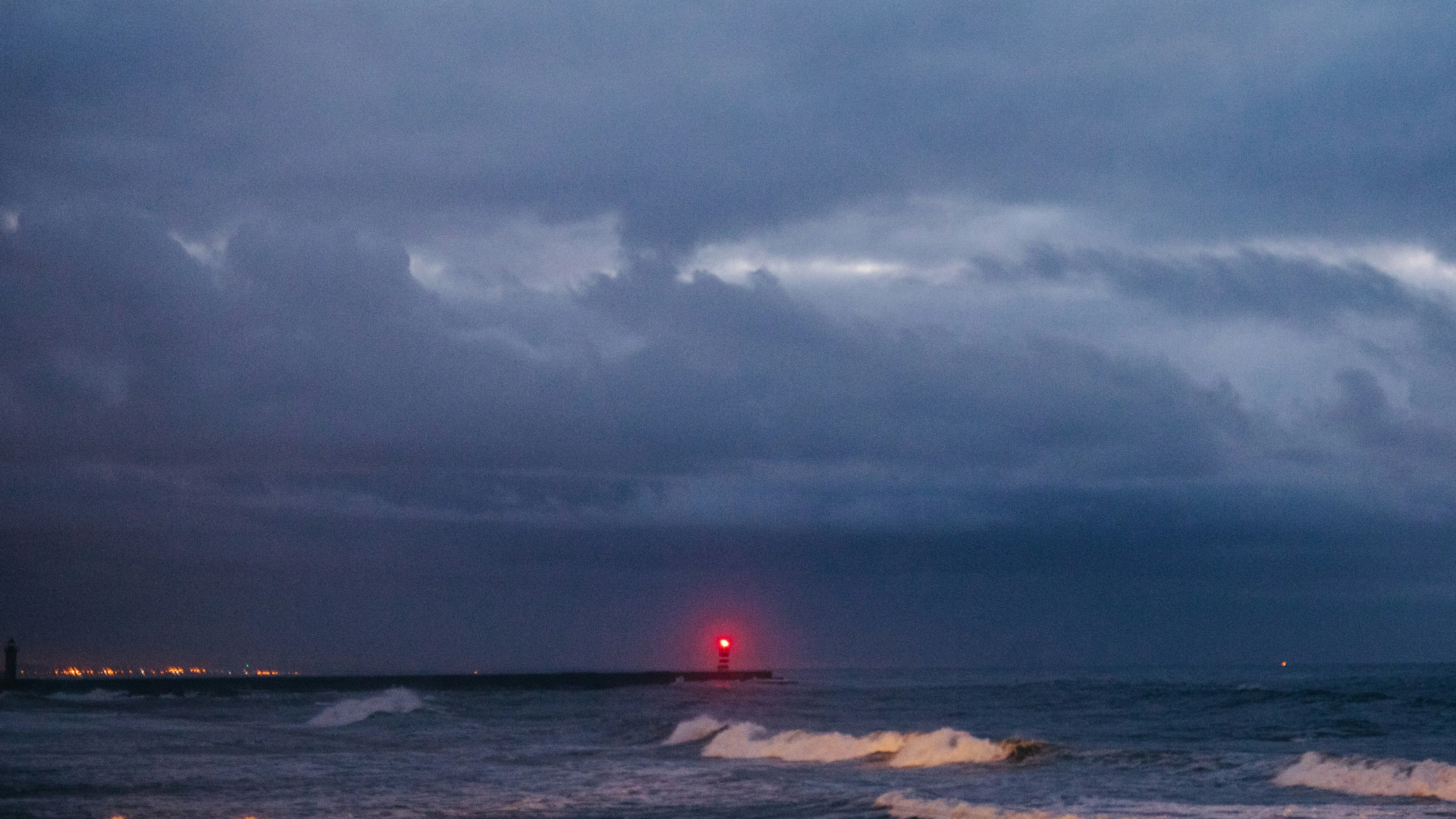 A lighthouse flashing red in the distance against a dark cloudy sky