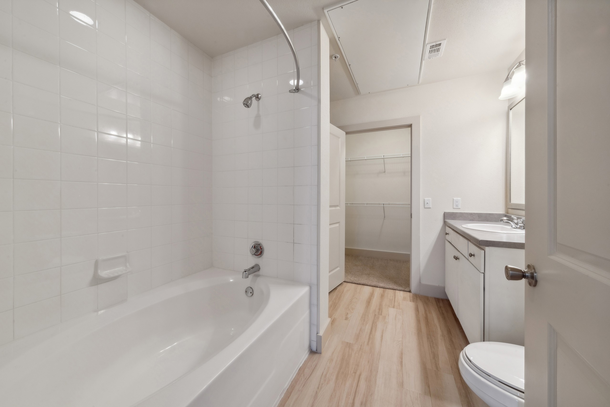 Bathroom at AMLI Park Avenue featuring a white bathtub with white tile surround and a white vanity with mirror and view into walk in closet