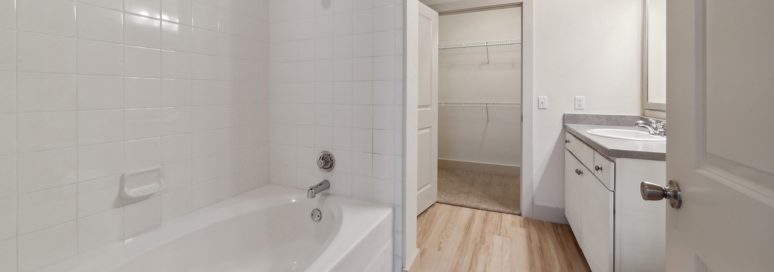 Bathroom at AMLI Park Avenue featuring a white bathtub with white tile surround and a white vanity with mirror and view into walk in closet
