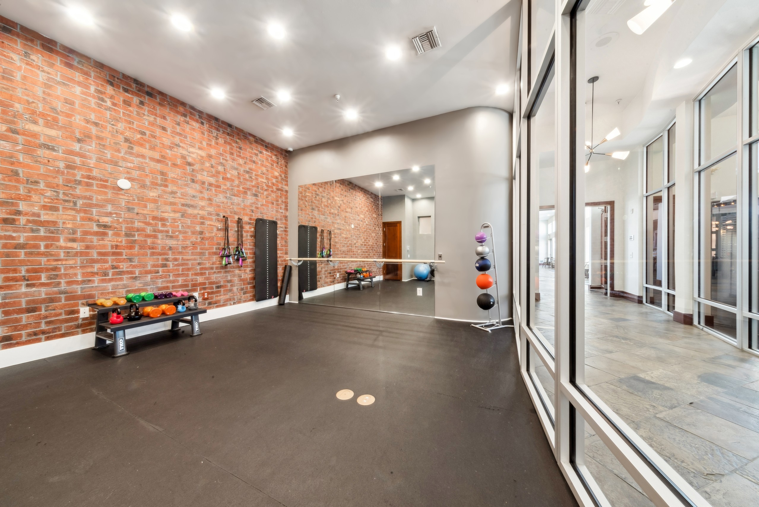 Yoga room at AMLI Park Avenue with exposed brick and a black floor and mirrored wall adjacent to a wall of interior windows