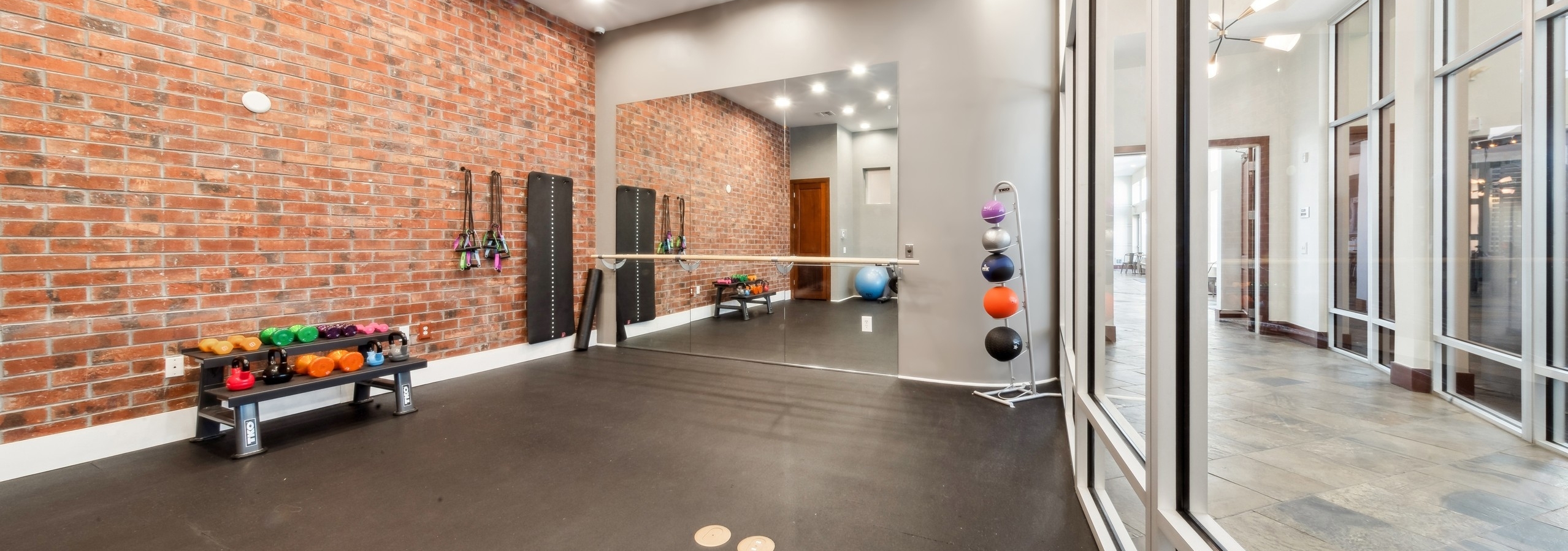 Yoga room at AMLI Park Avenue with exposed brick and a black floor and mirrored wall adjacent to a wall of interior windows