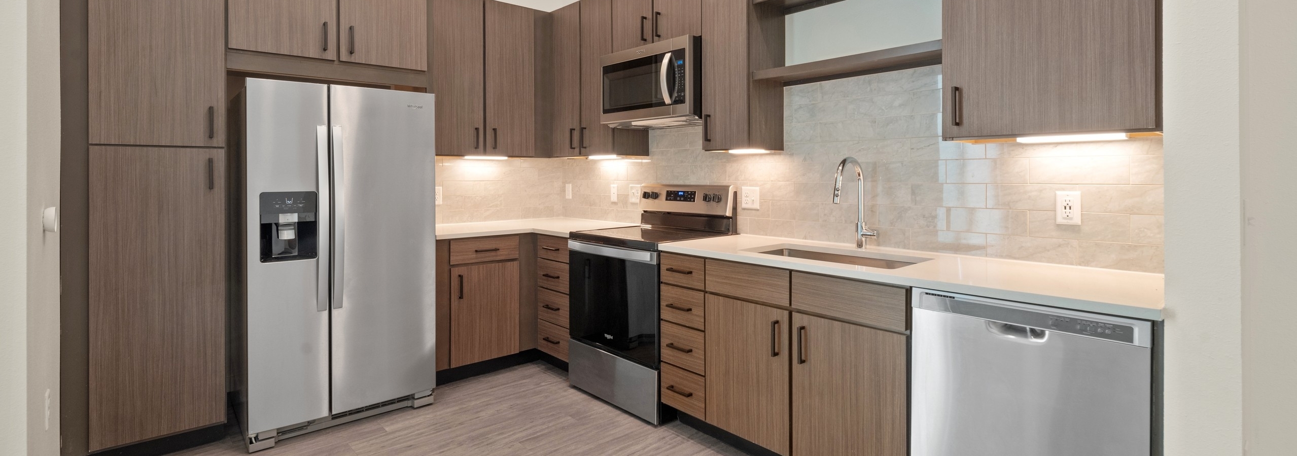 AMLI Art District kitchen with brown wood grain cabinets and light quartz countertops and stainless steel appliances on wood style floors