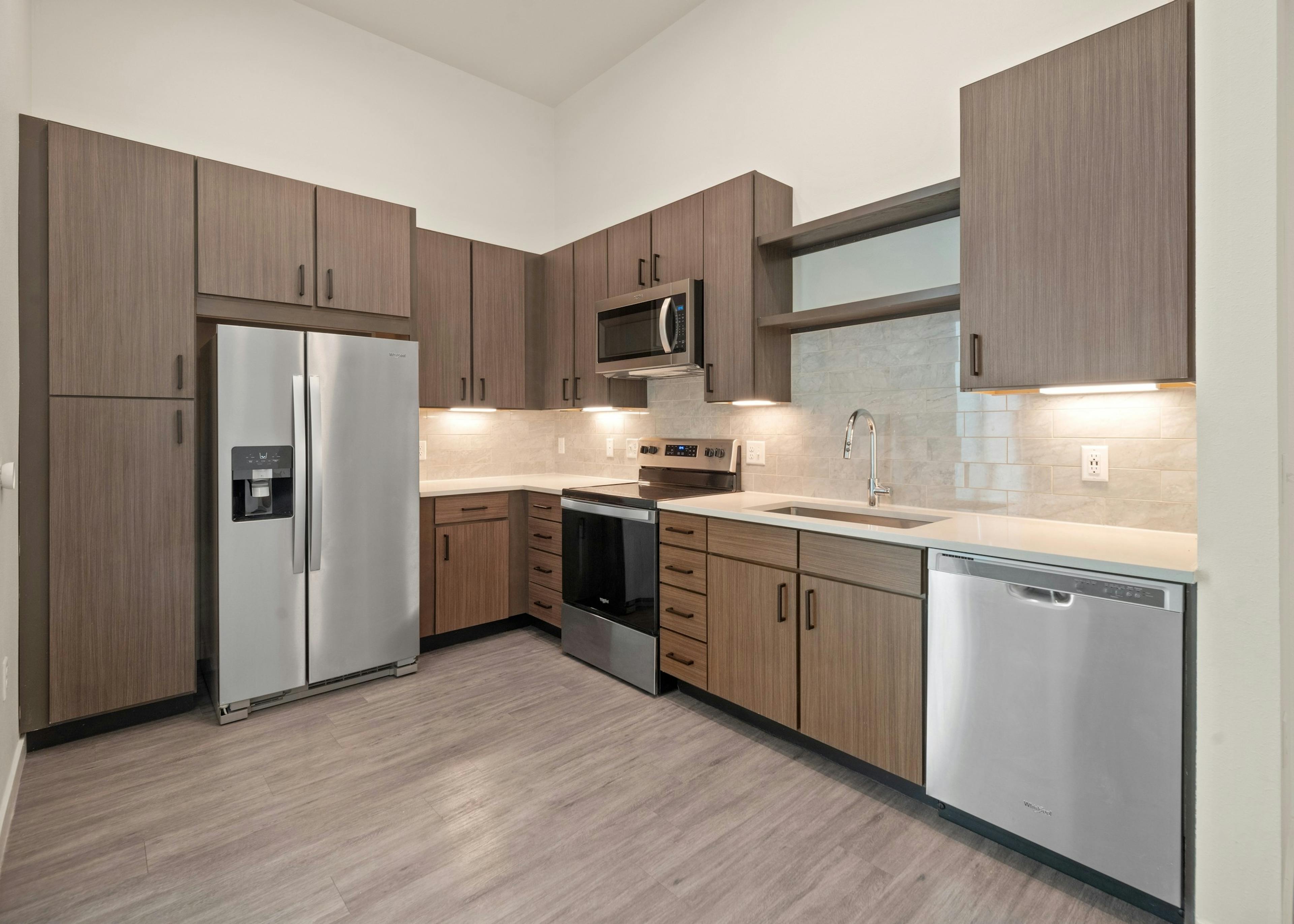 AMLI Art District kitchen with brown wood grain cabinets and light quartz countertops and stainless steel appliances on wood style floors