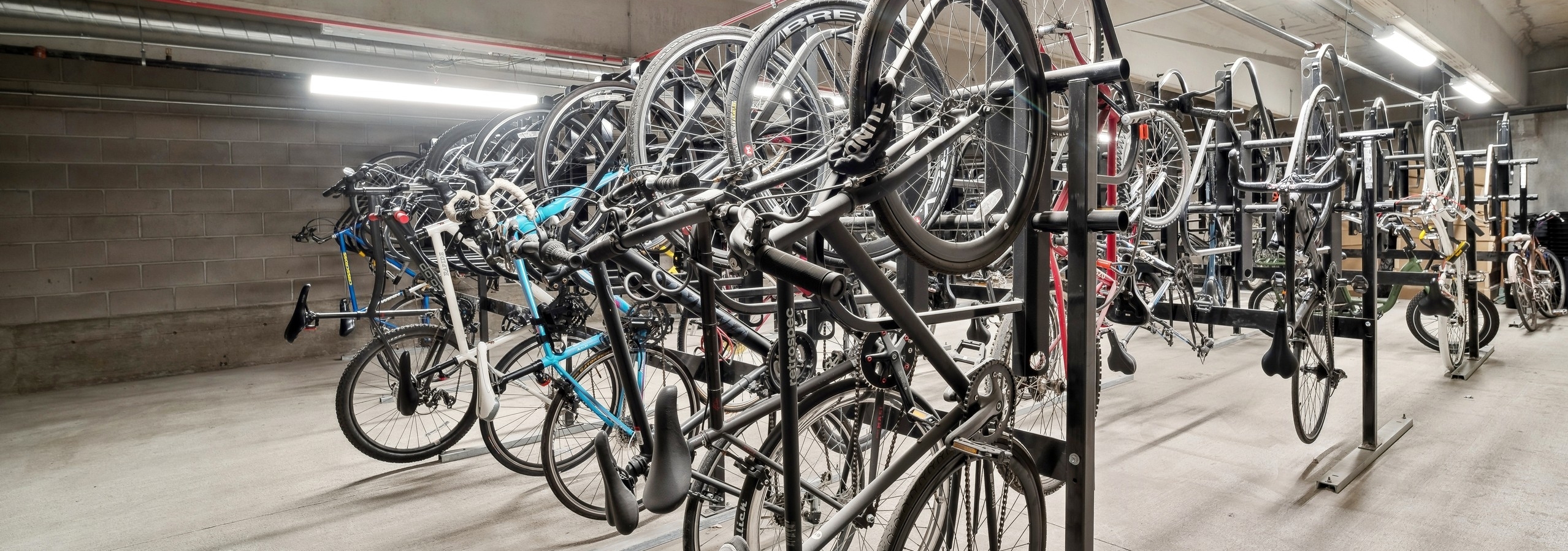 AMLI Art District indoor concrete bicycle storage room with multiple bikes mounted on vertical storage racks with overhead lighting