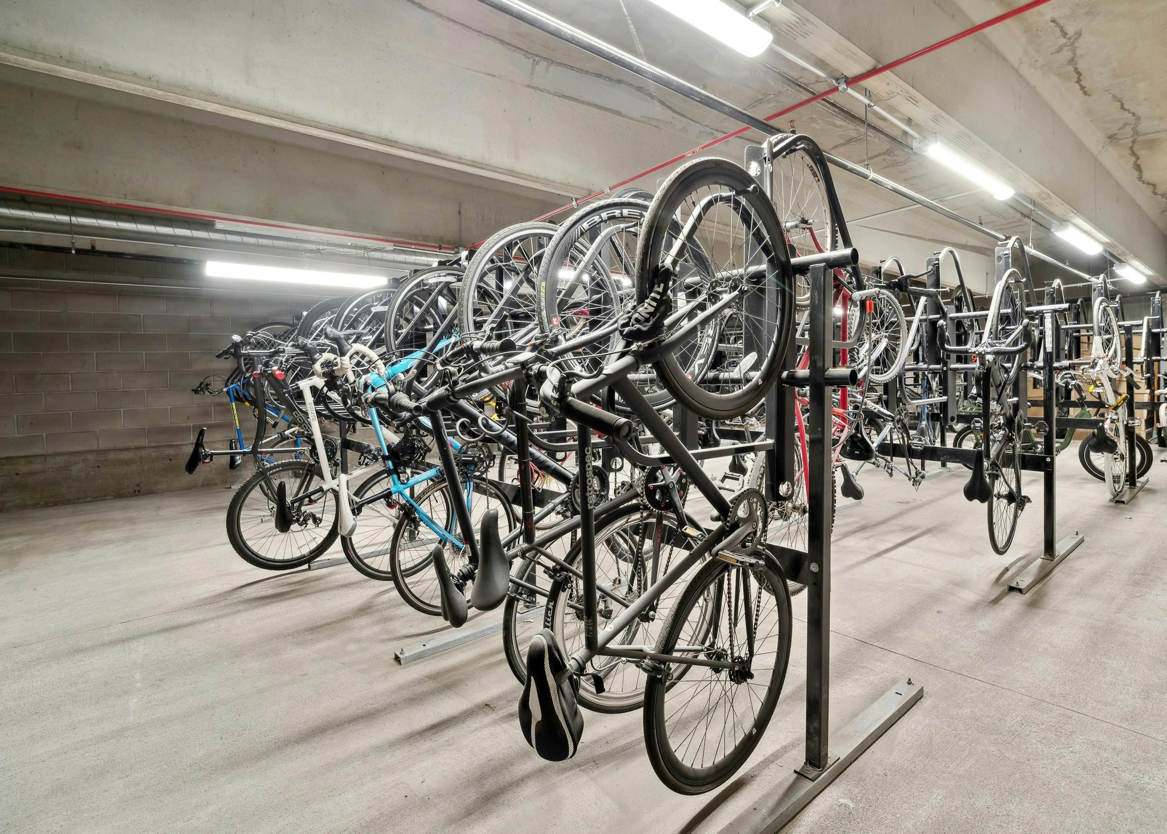 AMLI Art District indoor concrete bicycle storage room with multiple bikes mounted on vertical storage racks with overhead lighting