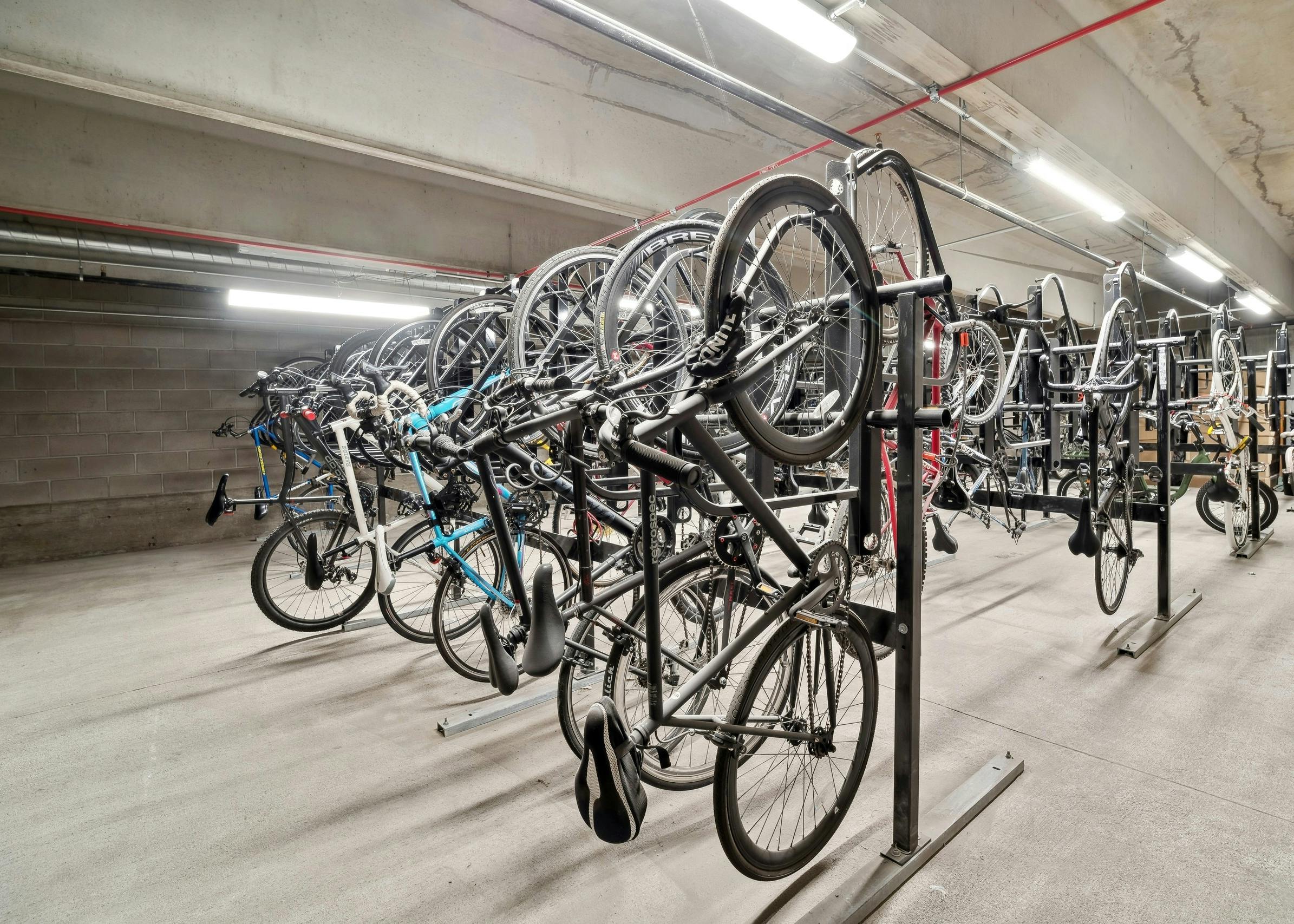 AMLI Art District indoor concrete bicycle storage room with multiple bikes mounted on vertical storage racks with overhead lighting