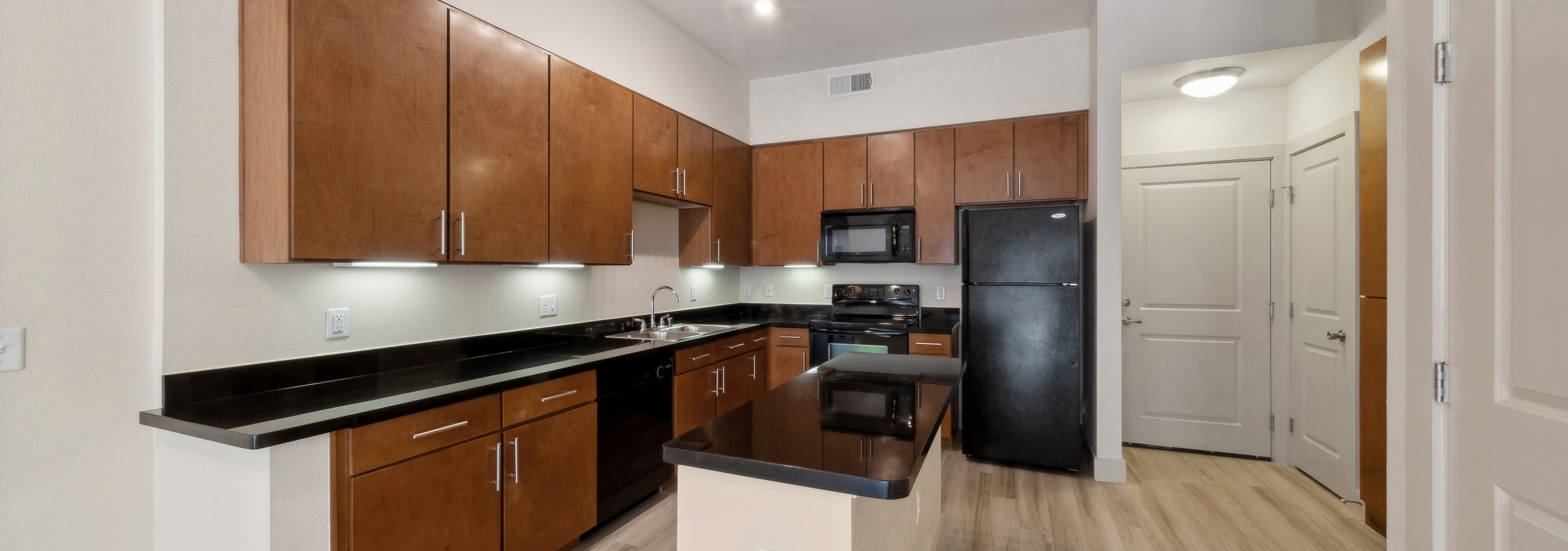Spacious island kitchen at AMLI Park Avenue with black countertops and wood cabinets and black appliances on wood style floors