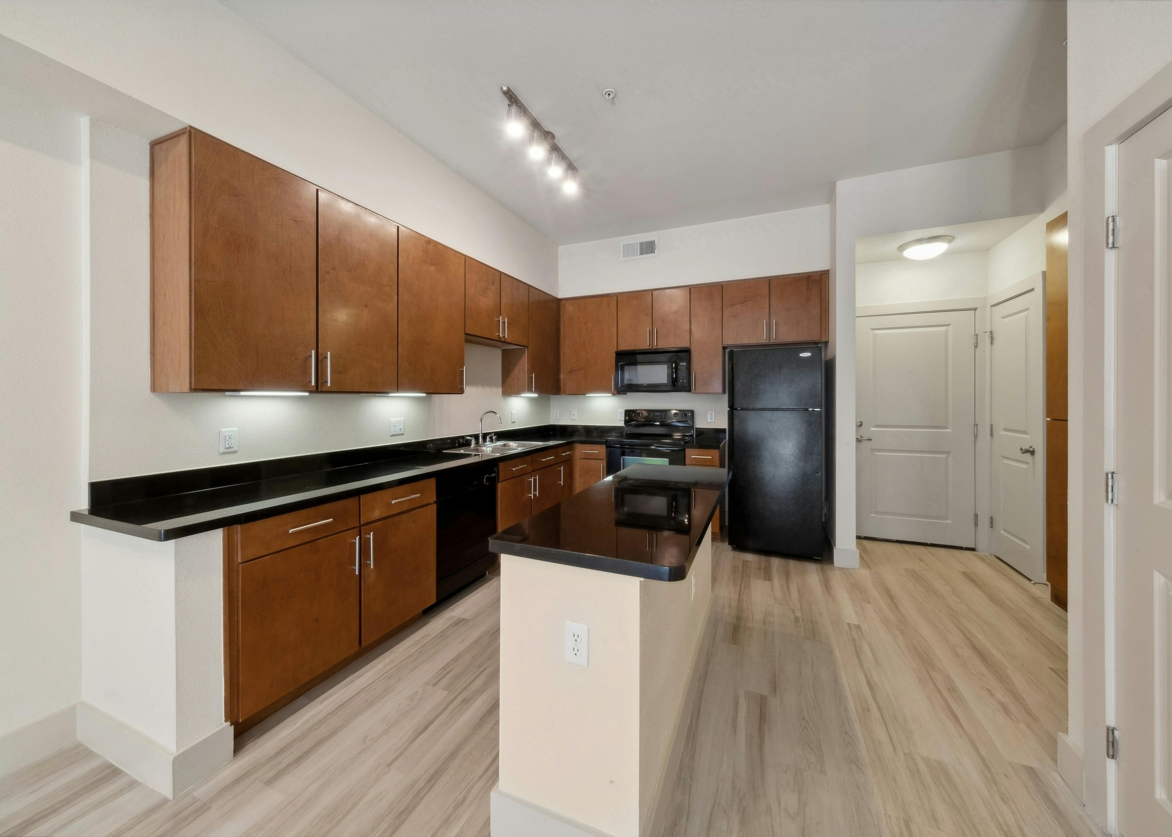 Spacious island kitchen at AMLI Park Avenue with black countertops and wood cabinets and black appliances on wood style floors