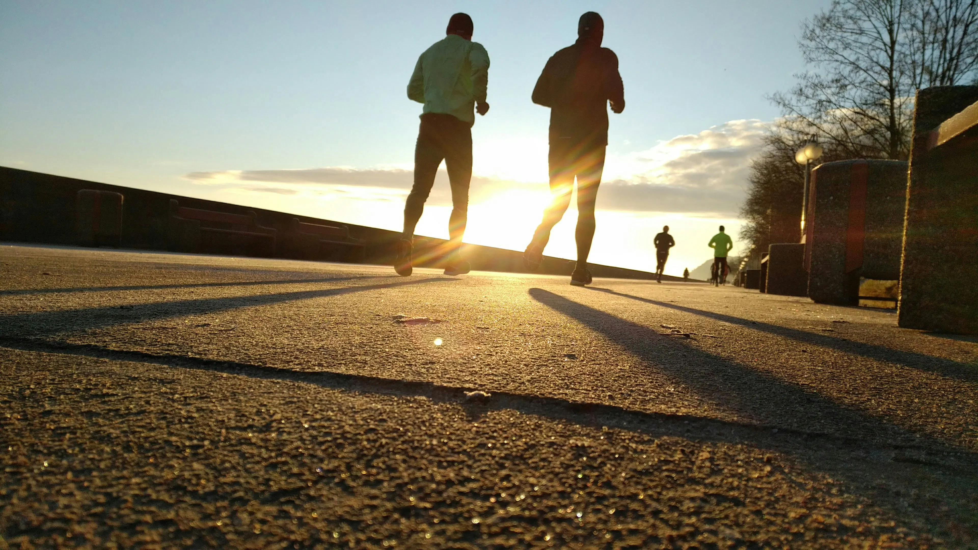Two joggers on a concrete sidewalk jogging toward the sunshine