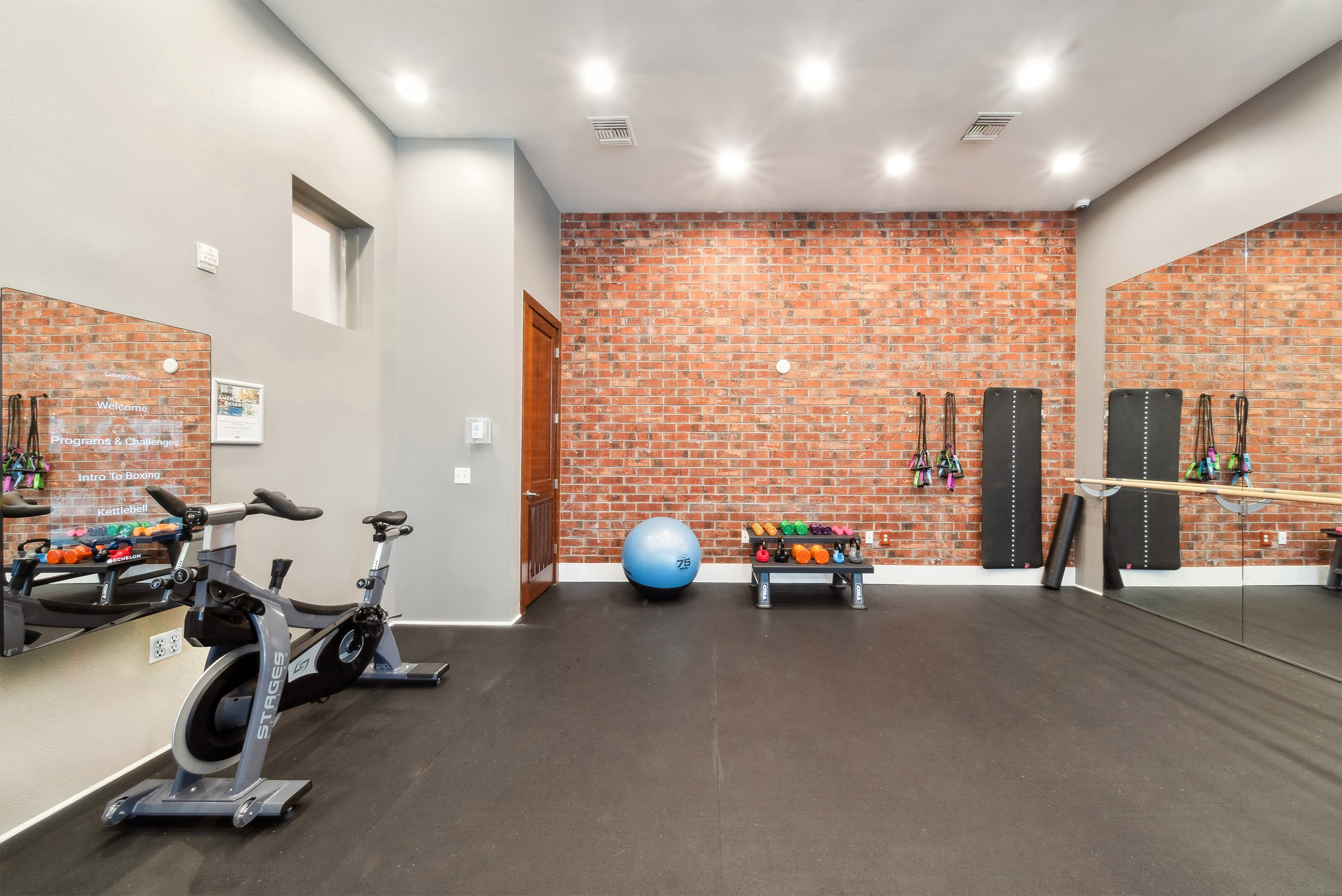 Yoga room at AMLI Park Avenue with exposed brick and a black floor and mirrored wall opposite video on demand