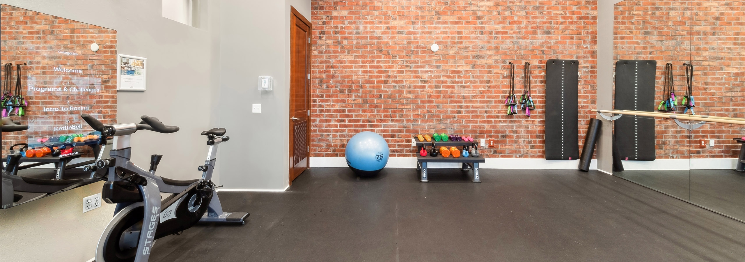 Yoga room at AMLI Park Avenue with exposed brick and a black floor and mirrored wall opposite video on demand