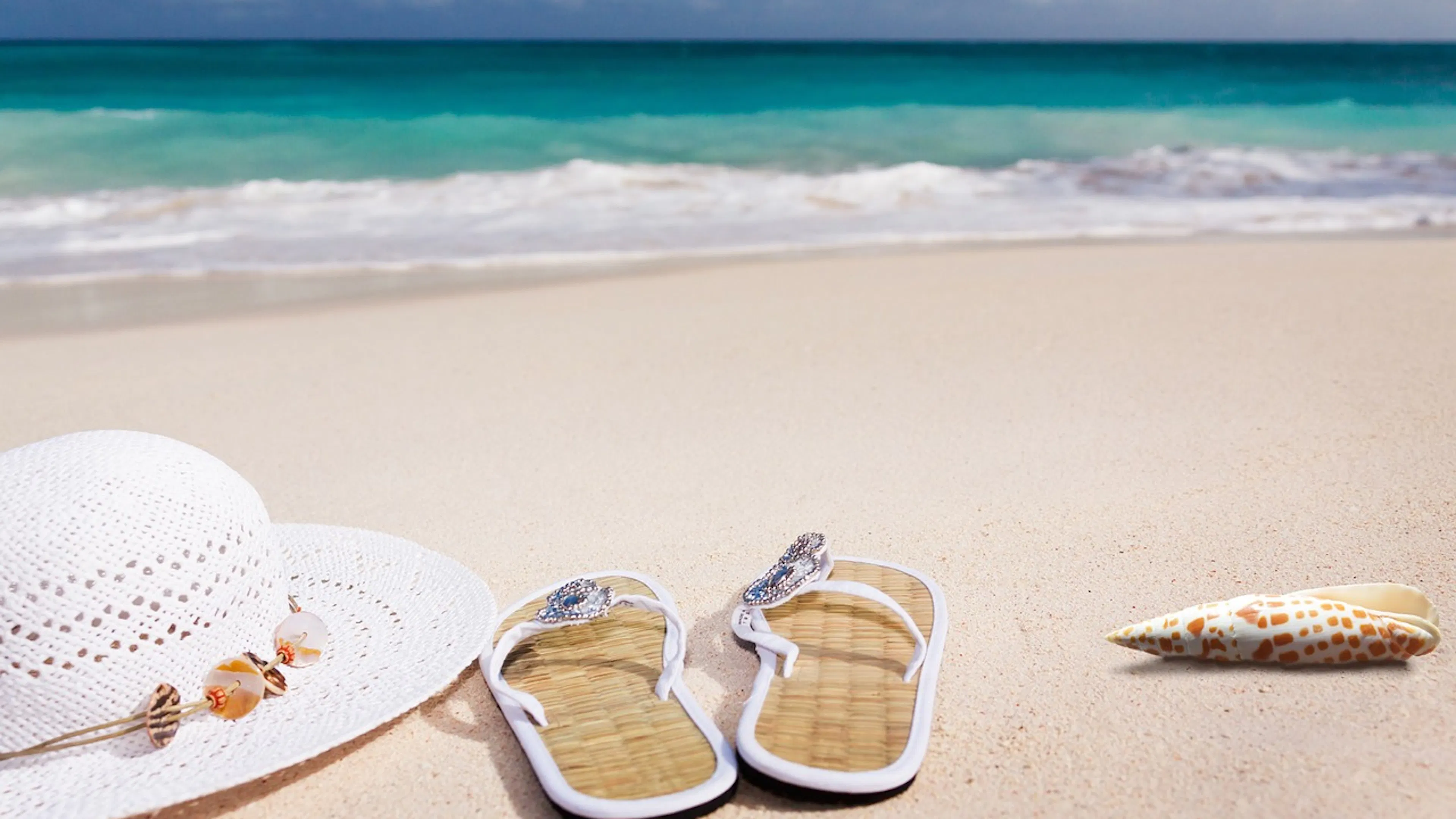 white hat, sandals and shell on sandy beach with blue water