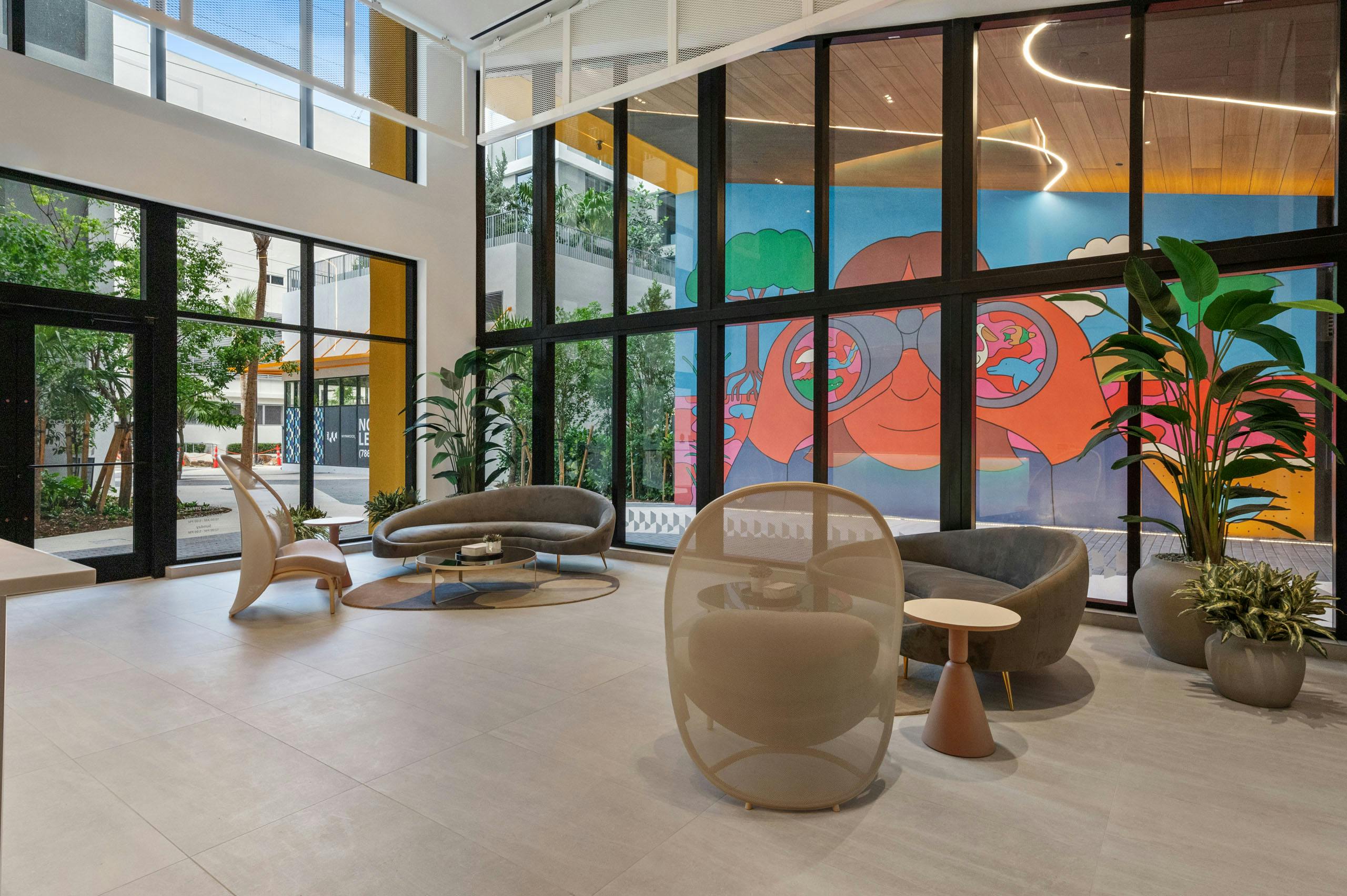 A spacious lobby at AMLI Wynwood with designer furniture and large windows overlooking a colorful mural