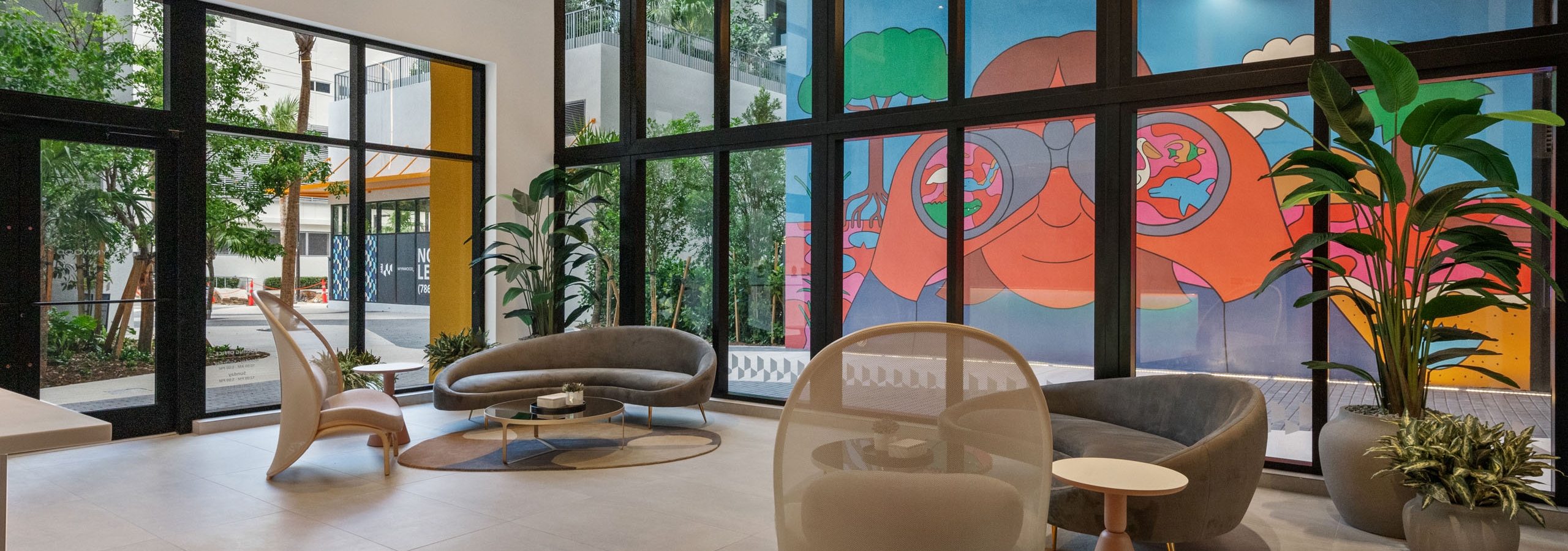 A spacious lobby at AMLI Wynwood with designer furniture and large windows overlooking a colorful mural