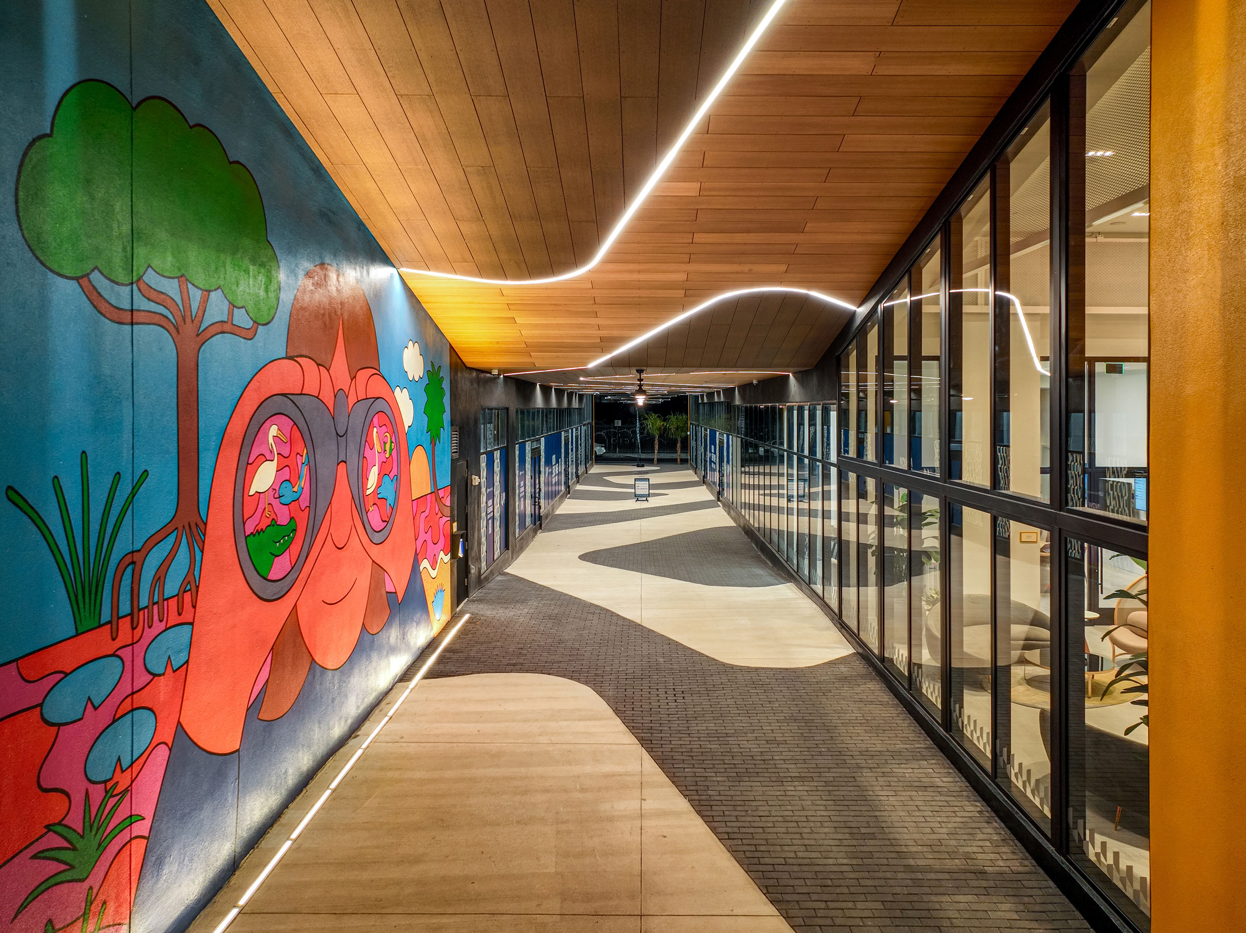 Walkway at AMLI Wynwood apartments with glass windows of the lobby looking out to a colorful mural and zigzag brick floor pattern