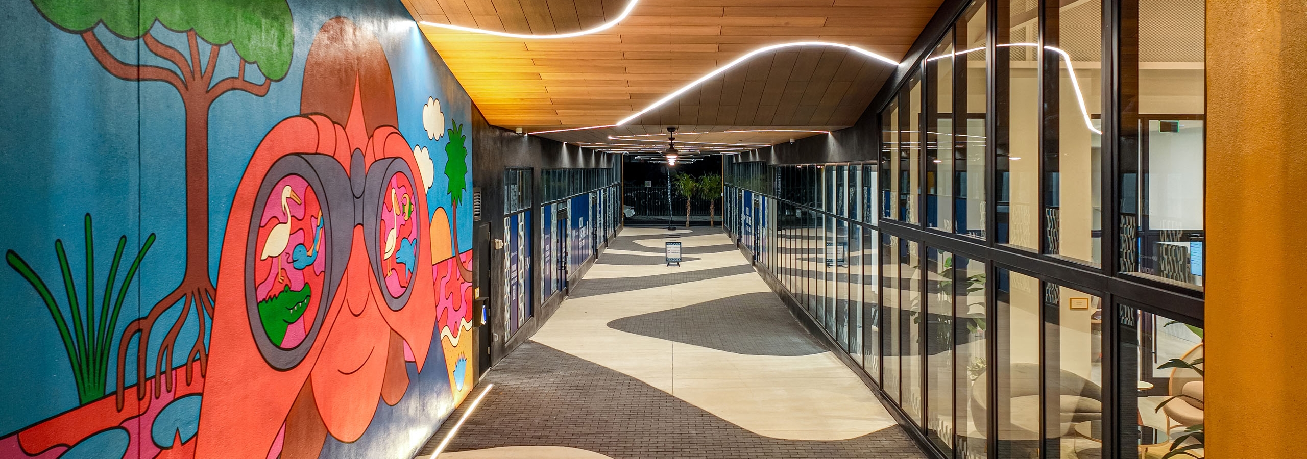 Walkway at AMLI Wynwood apartments with glass windows of the lobby looking out to a colorful mural and zigzag brick floor pattern