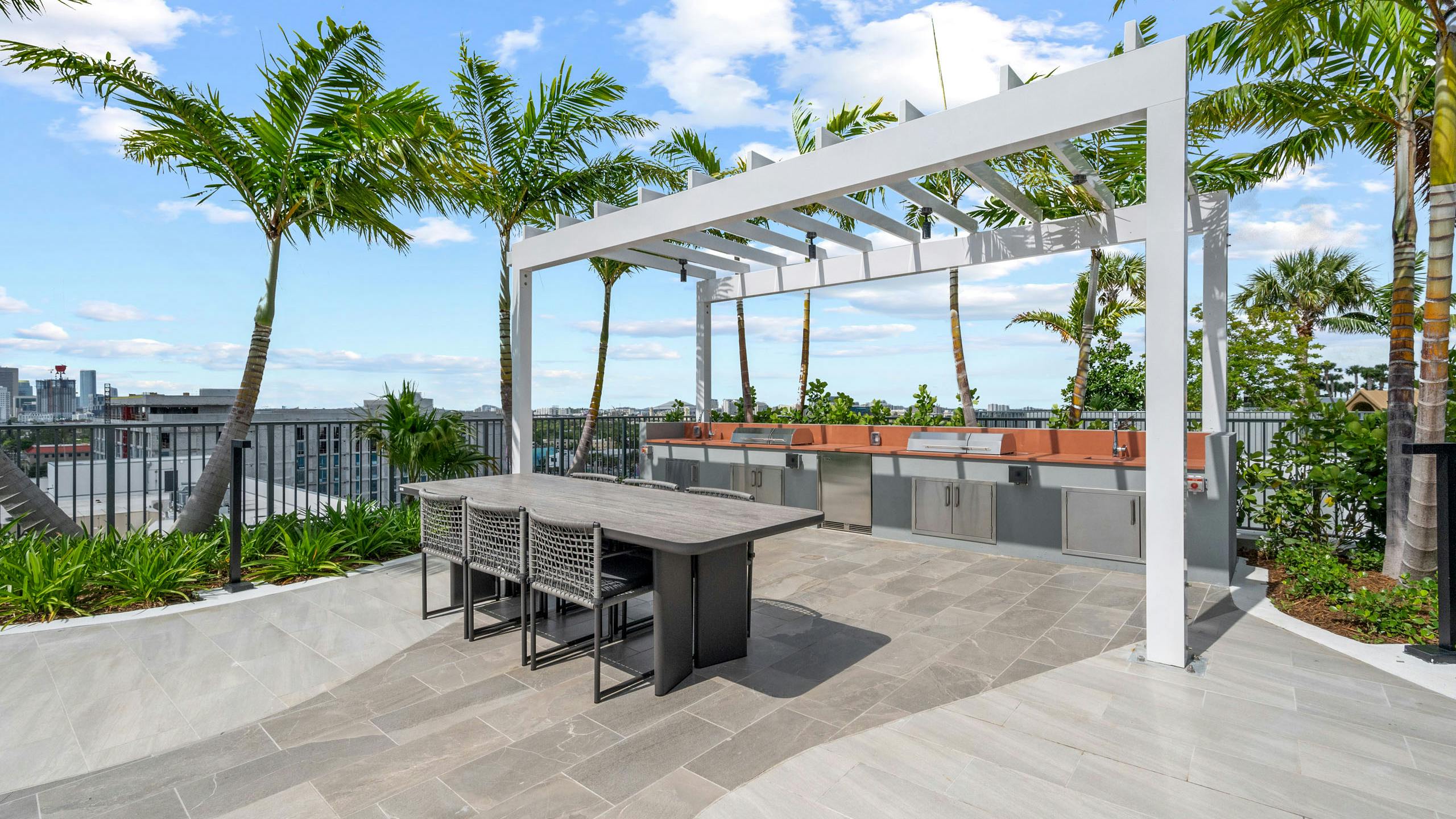 A daytime view of a covered area at AMLI Wynwood apartments with two large grills built into an outdoor kitchen counter and a dining table