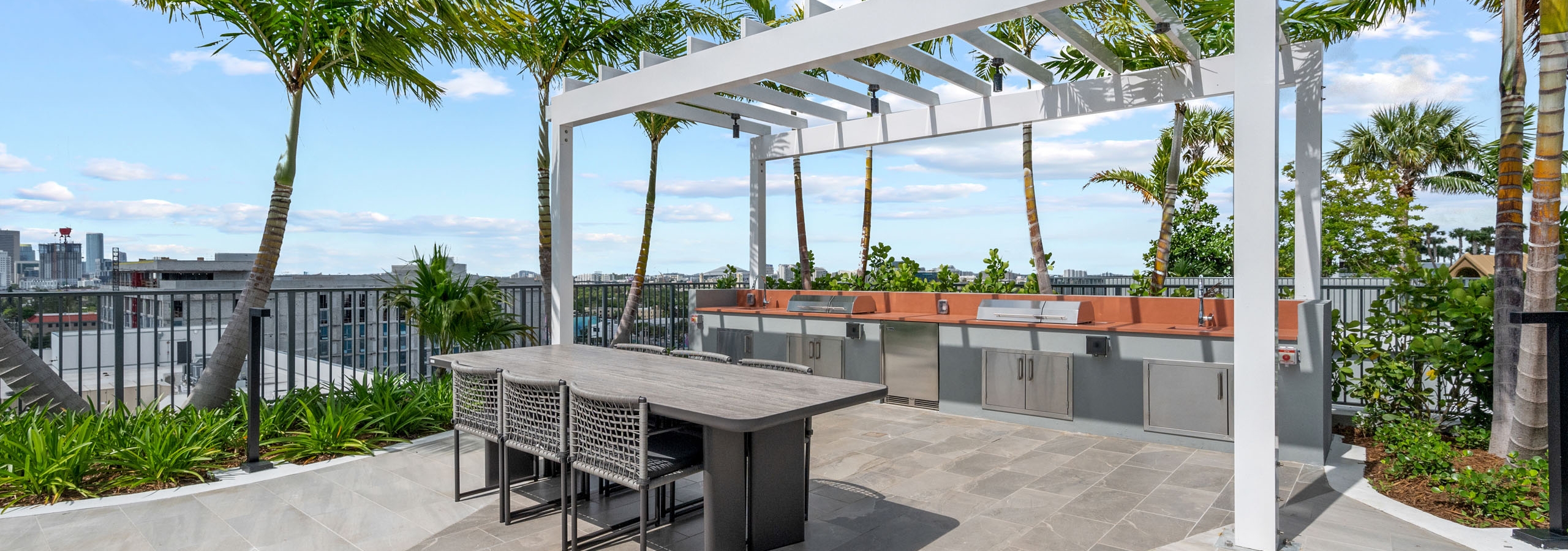 A daytime view of a covered area at AMLI Wynwood apartments with two large grills built into an outdoor kitchen counter and a dining table