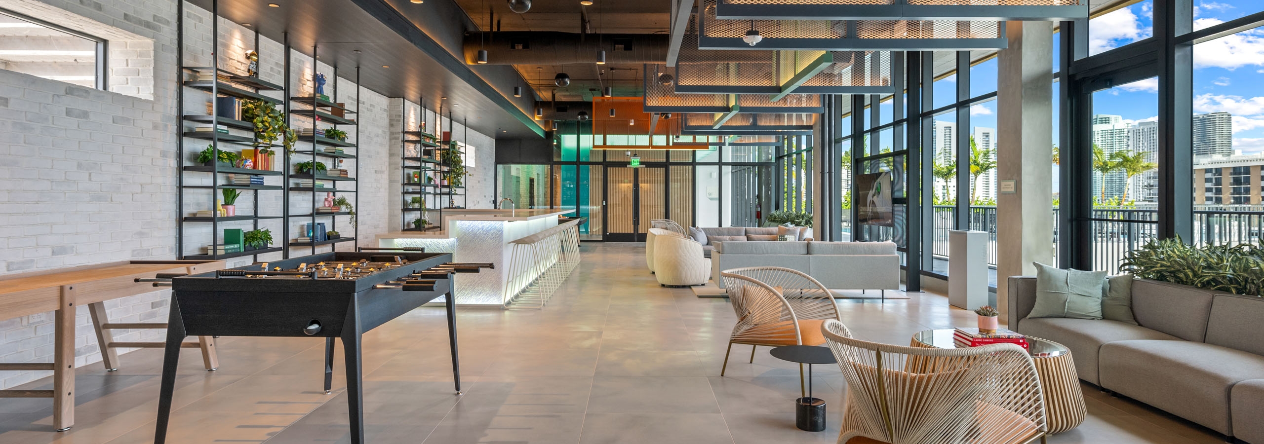 Sky lounge at AMLI Wynwood with industrial lighting and foosball next to an illuminated bar top and designer tables and chairs