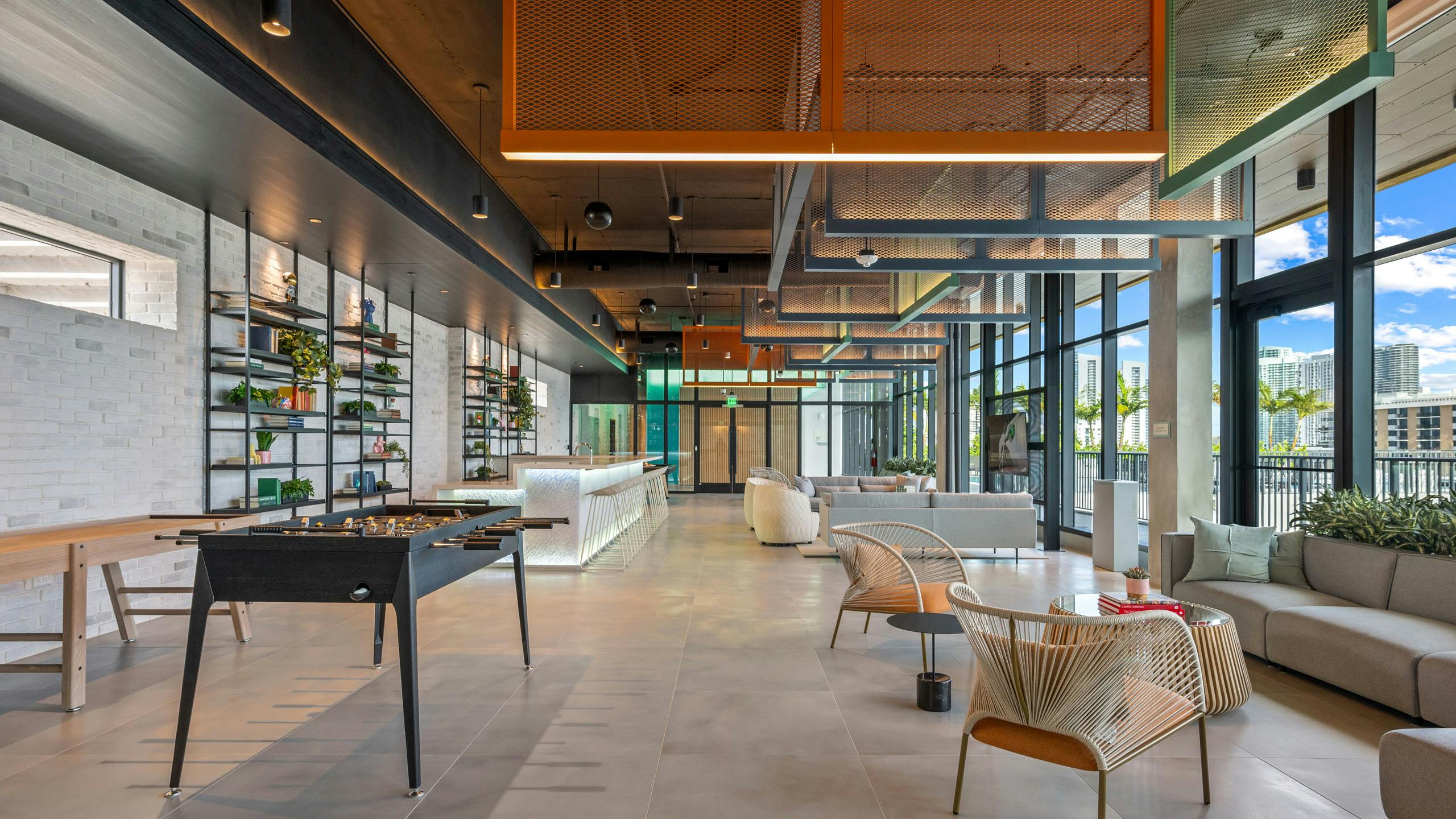 Sky lounge at AMLI Wynwood with industrial lighting and foosball next to an illuminated bar top and designer tables and chairs