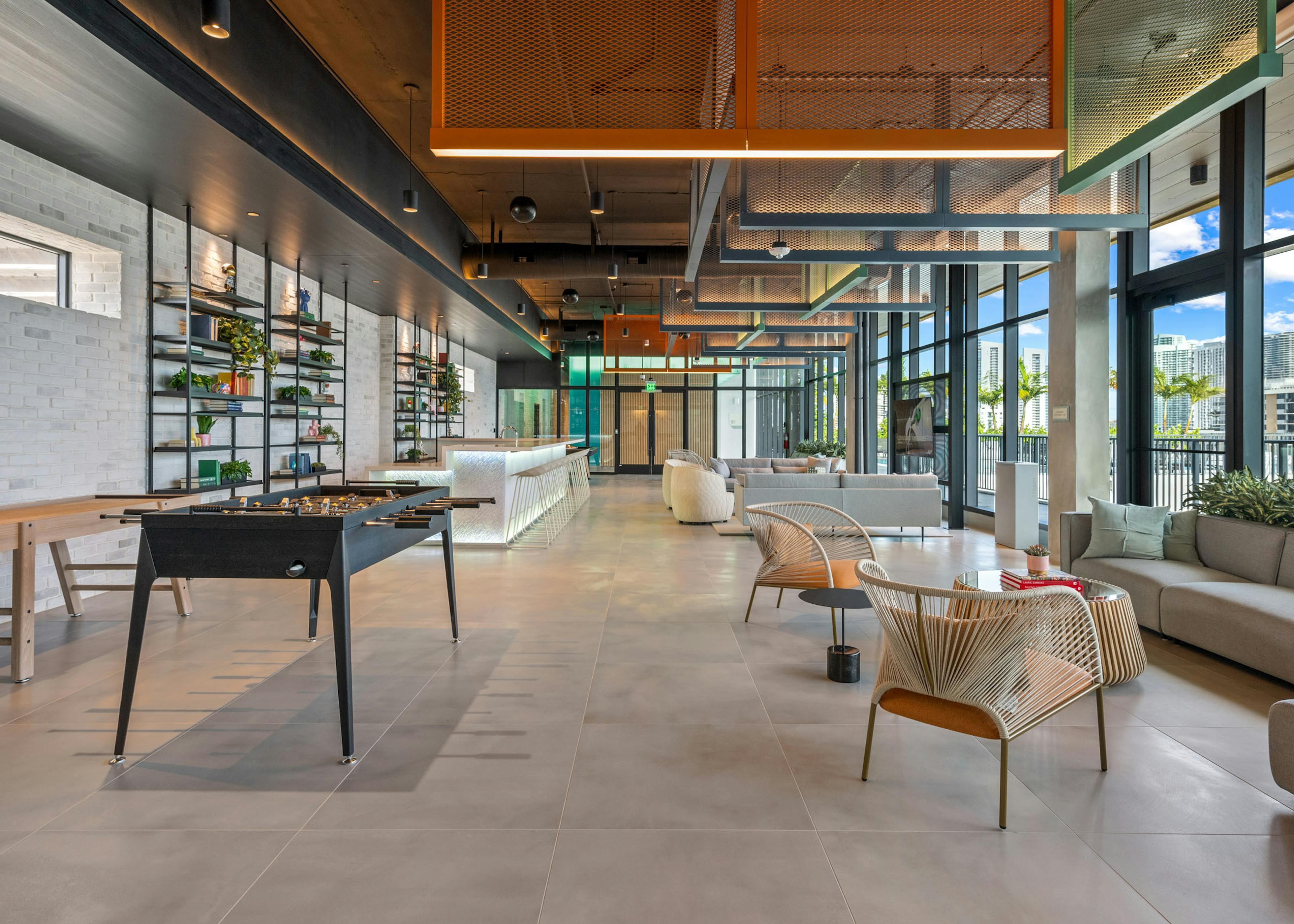 Sky lounge at AMLI Wynwood with industrial lighting and foosball next to an illuminated bar top and designer tables and chairs