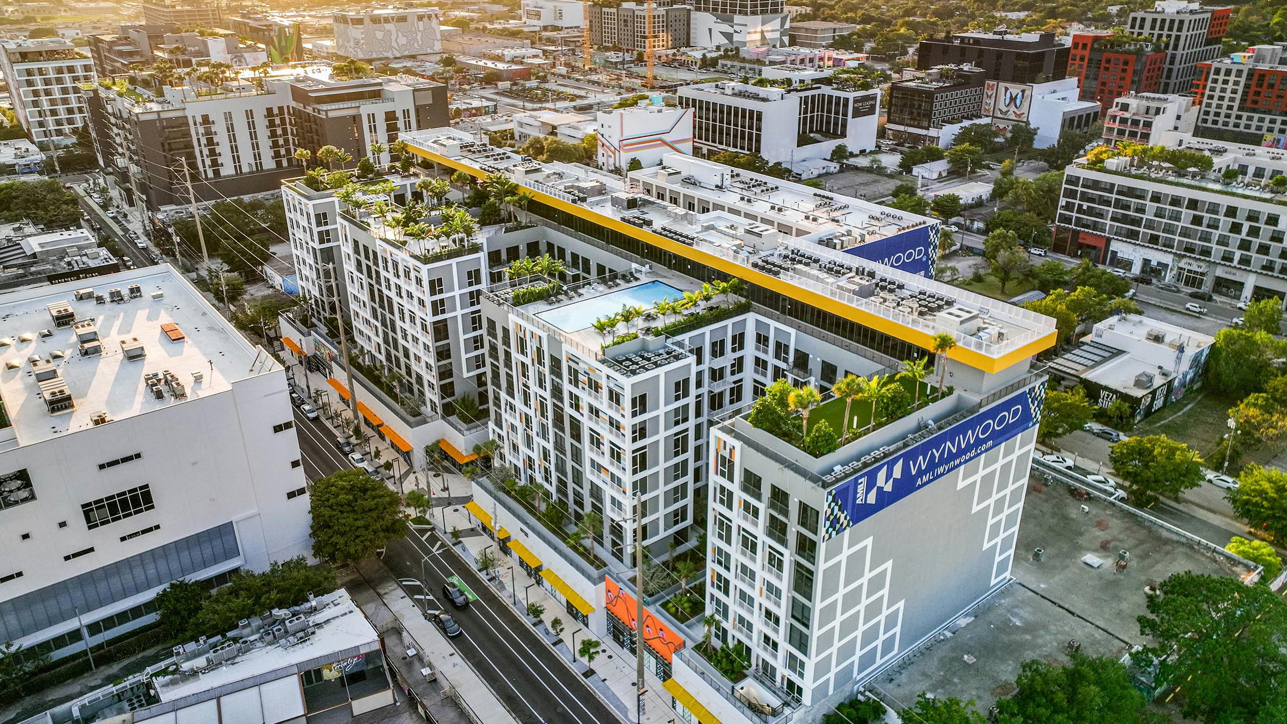 Aerial view of a modern multistory building at AMLI Wynwood apartments with large blue banners surrounded by a cityscape