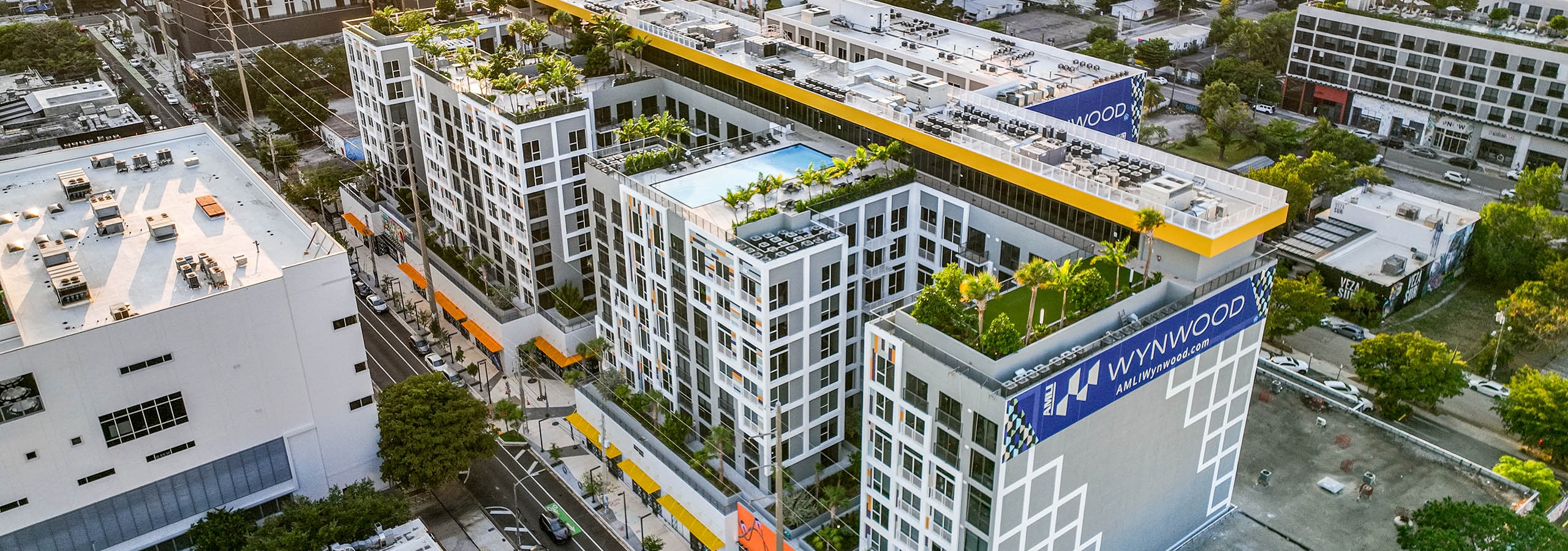 Aerial view of a modern multistory building at AMLI Wynwood apartments with large blue banners surrounded by a cityscape