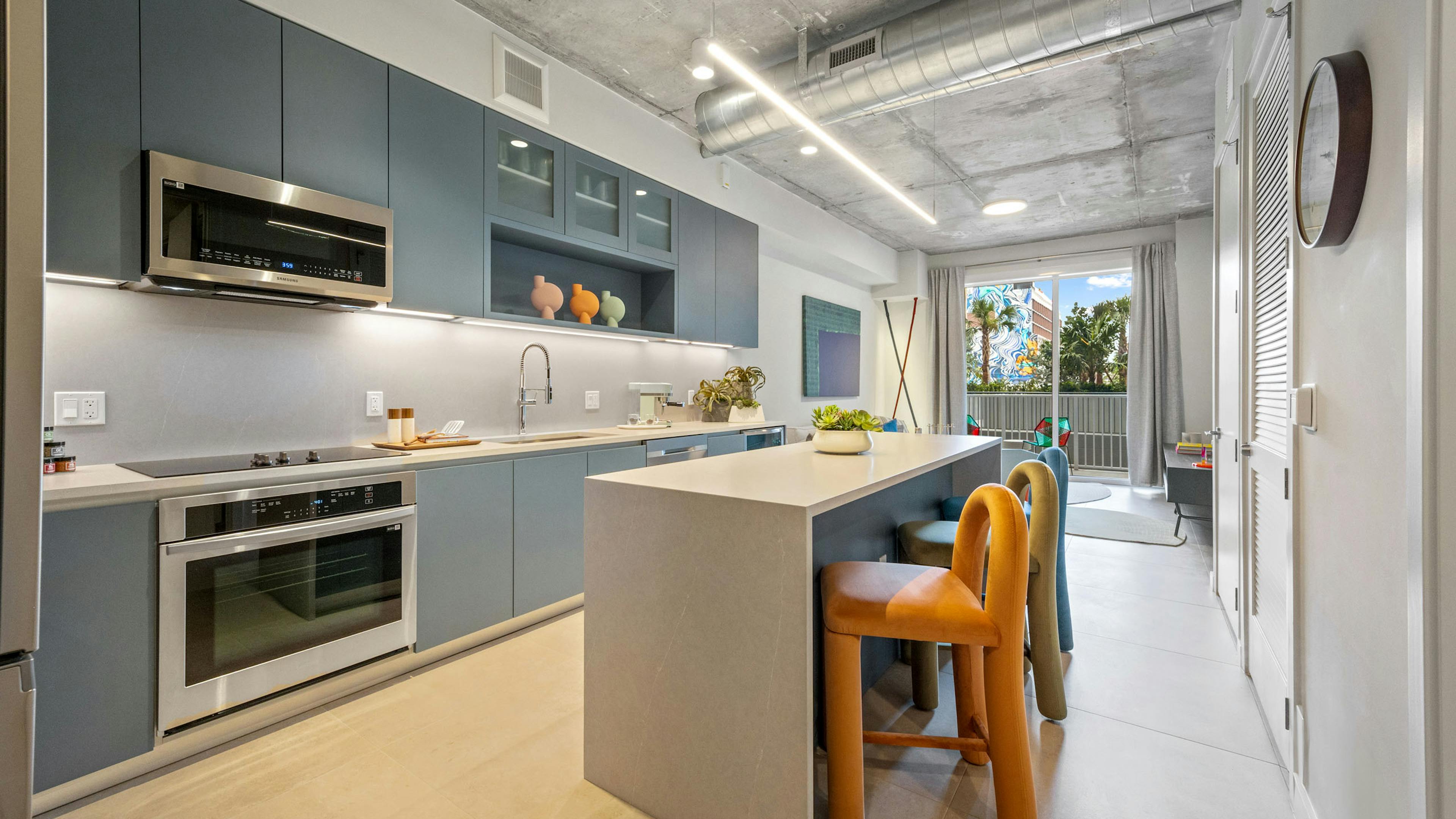 AMLI Wynwood apartment kitchen looking out to a living room and patio with a daytime view of clouds and a colorful building mural