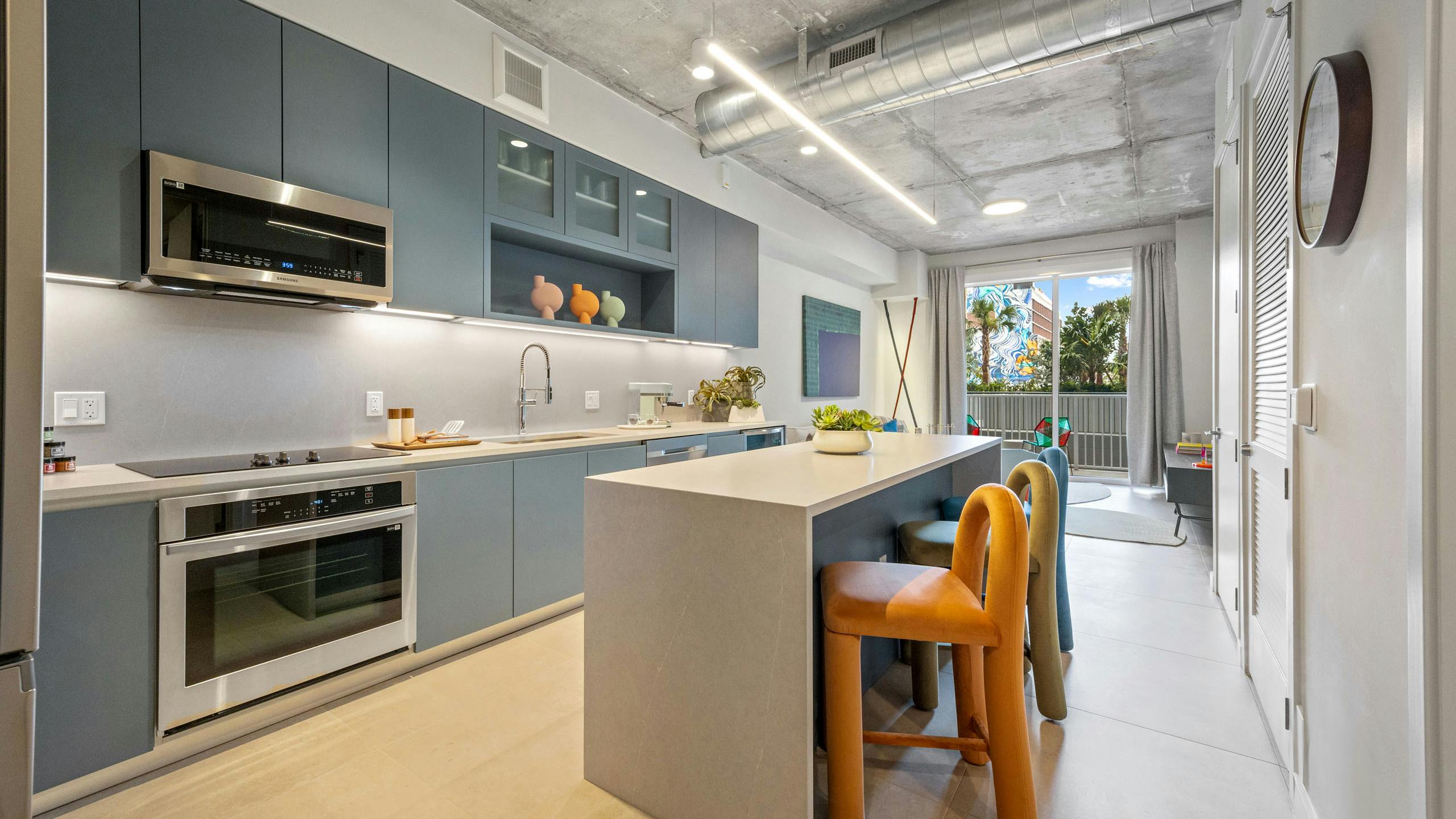 AMLI Wynwood apartment kitchen looking out to a living room and patio with a daytime view of clouds and a colorful building mural