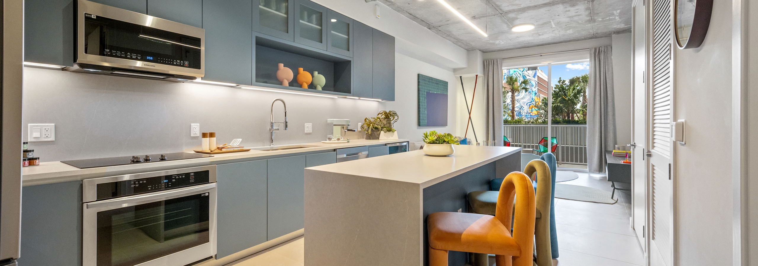 AMLI Wynwood apartment kitchen looking out to a living room and balcony with a daytime view of clouds and a colorful building mural