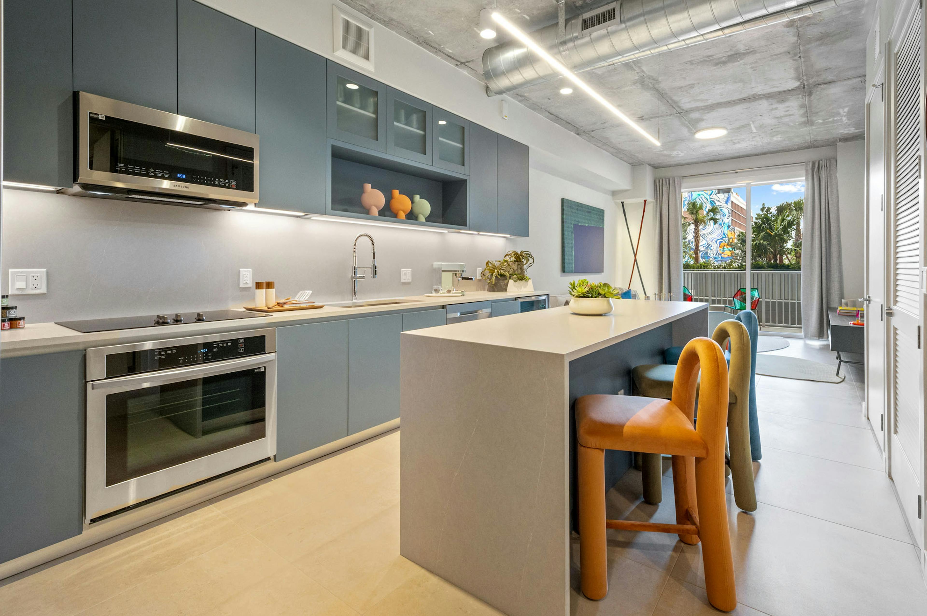AMLI Wynwood apartment kitchen looking out to a living room and patio with a daytime view of clouds and a colorful building mural