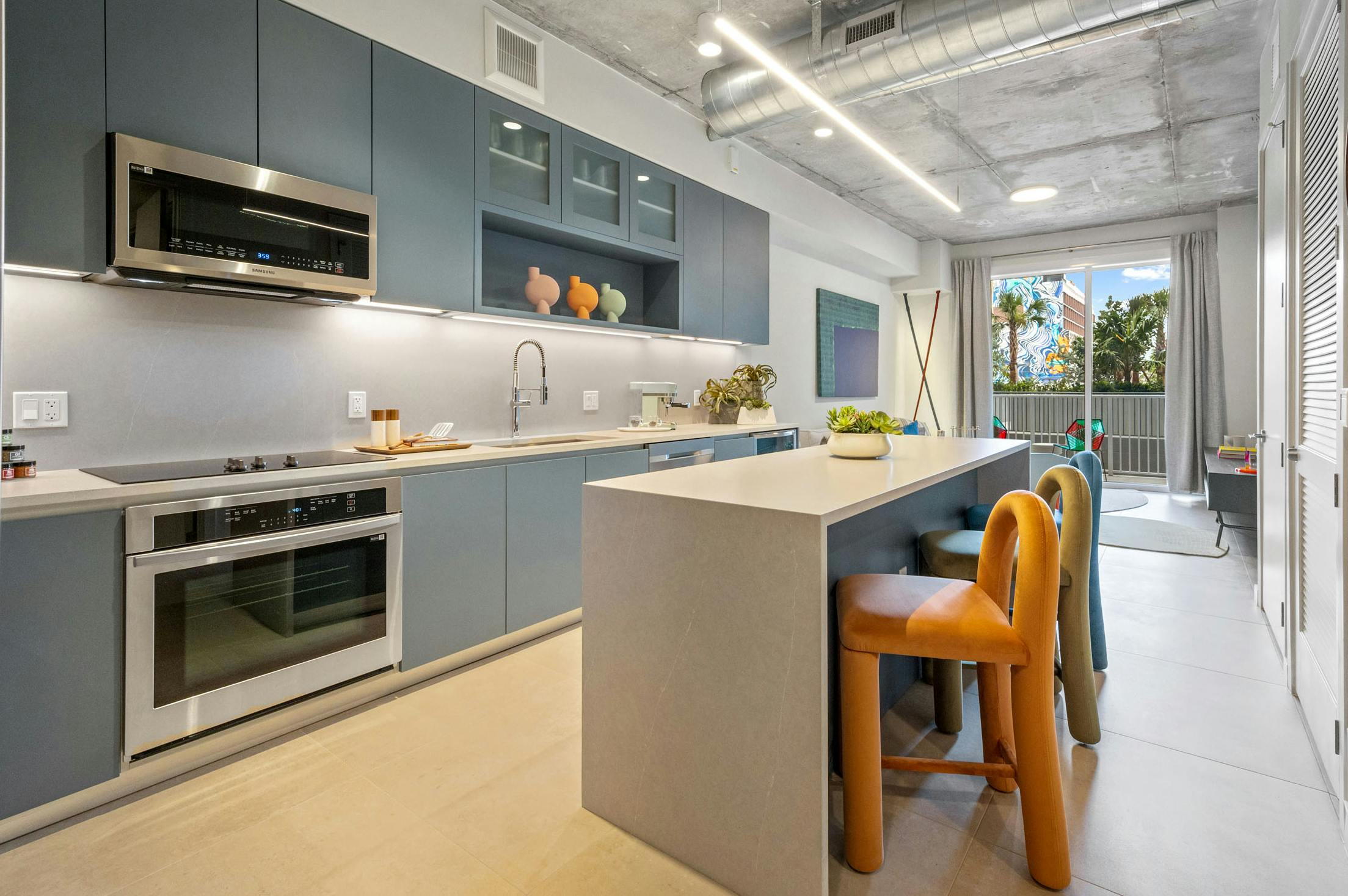 AMLI Wynwood apartment kitchen looking out to a living room and patio with a daytime view of clouds and a colorful building mural
