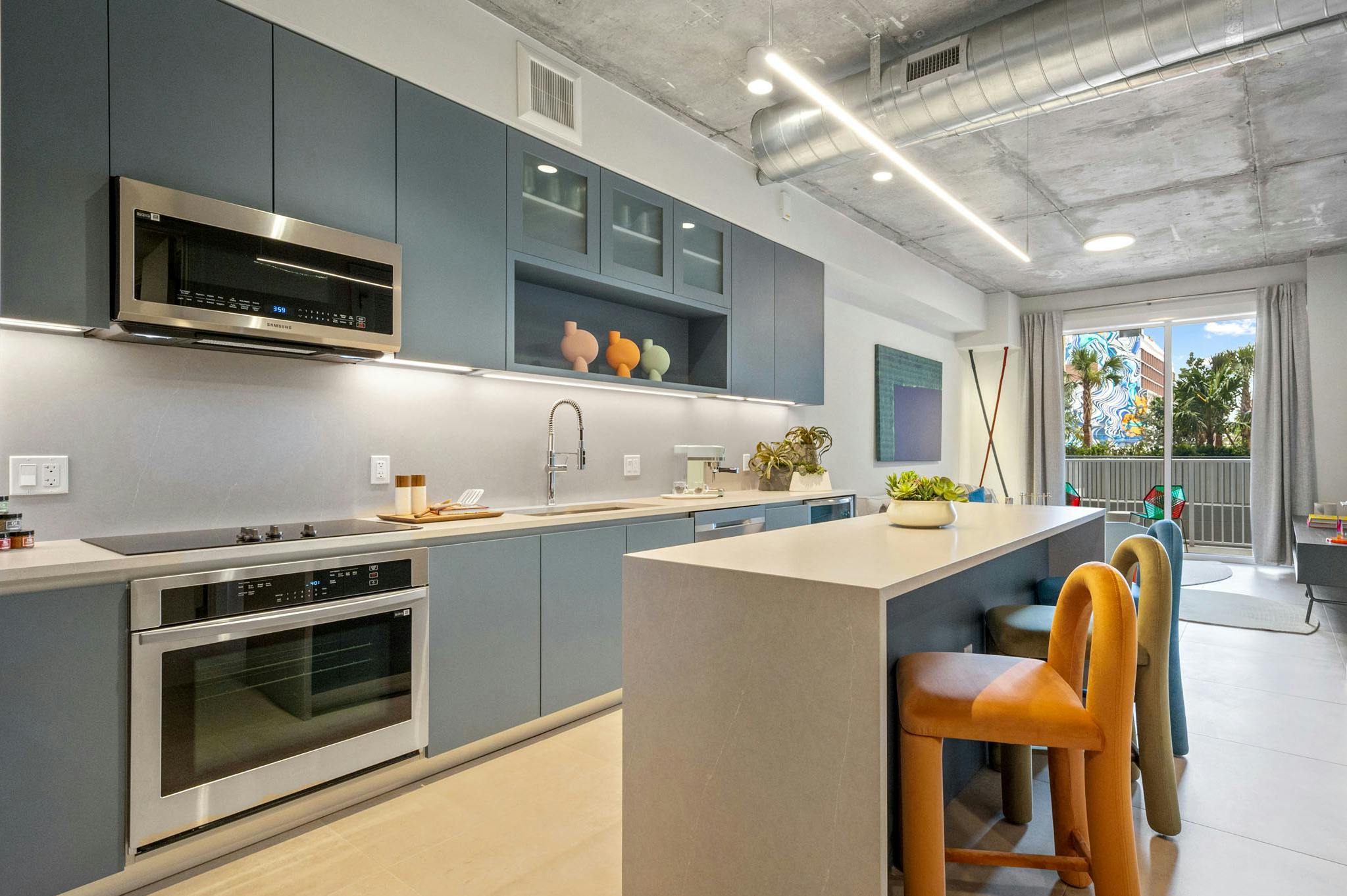 AMLI Wynwood apartment kitchen looking out to a living room and patio with a daytime view of clouds and a colorful building mural