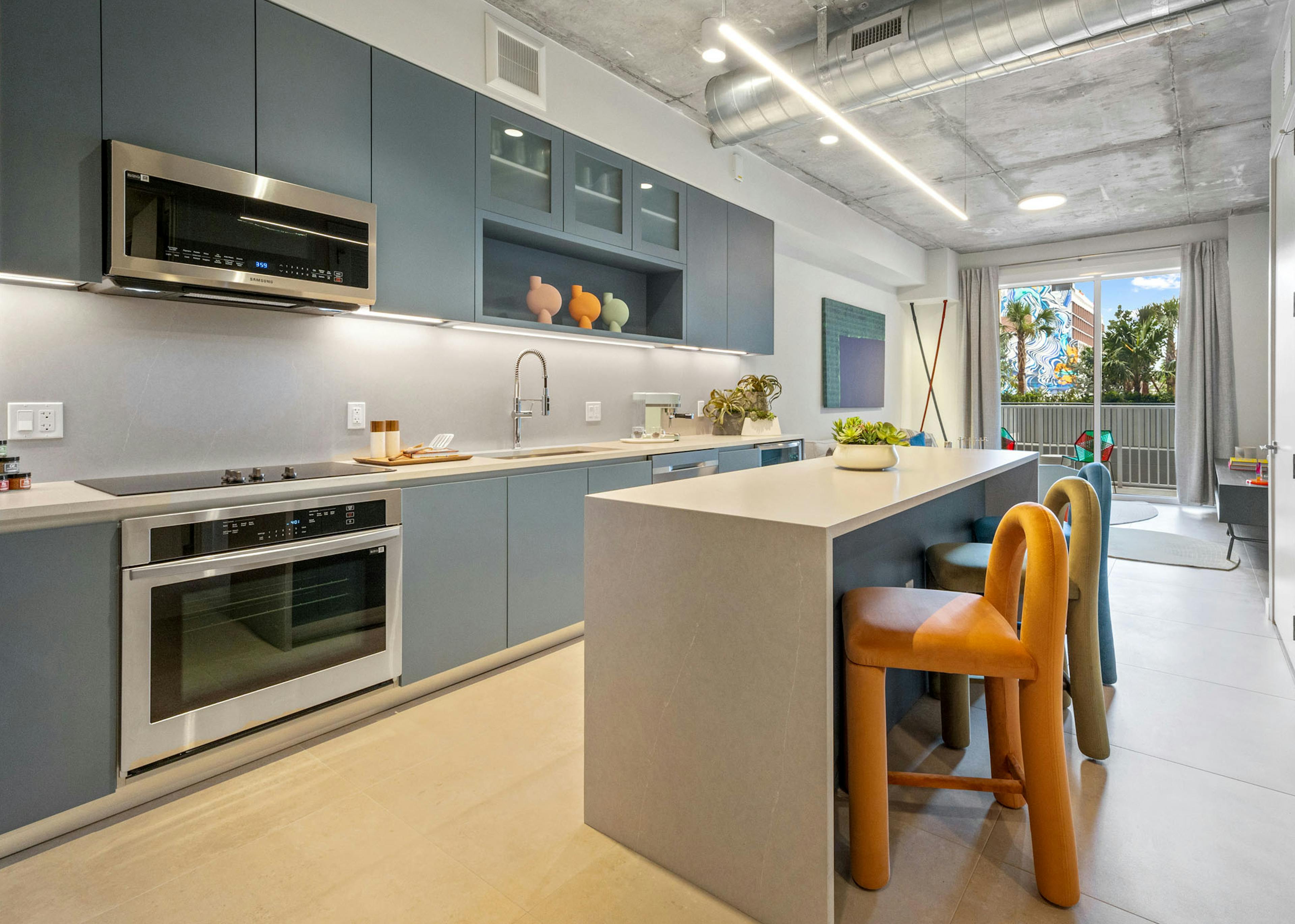 AMLI Wynwood apartment kitchen looking out to a living room and patio with a daytime view of clouds and a colorful building mural