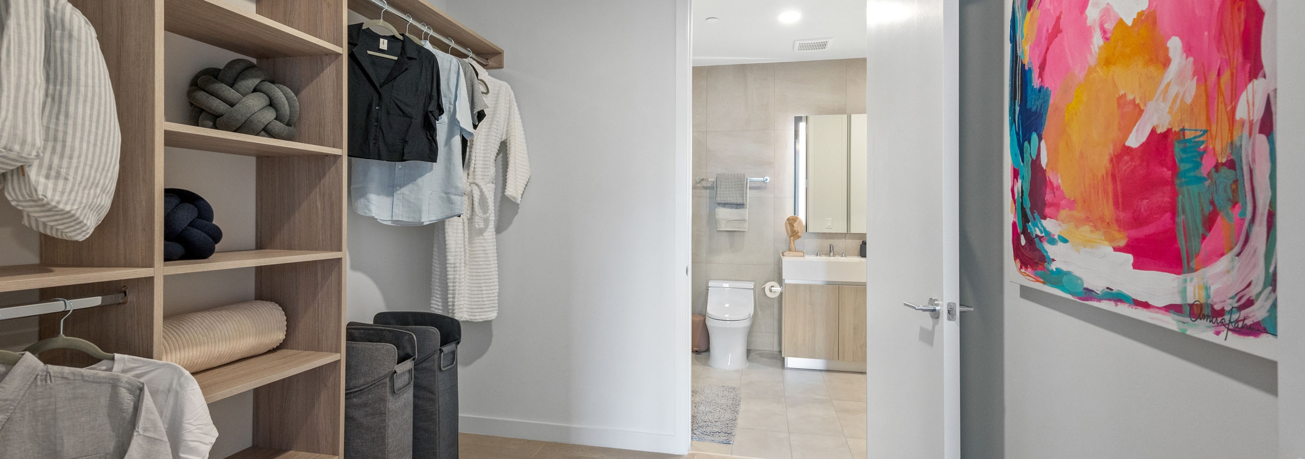 A large walk in closet at AMLI Wynwood apartments leading to a modern bathroom with wooden shelving showing clothing and laundry hampers