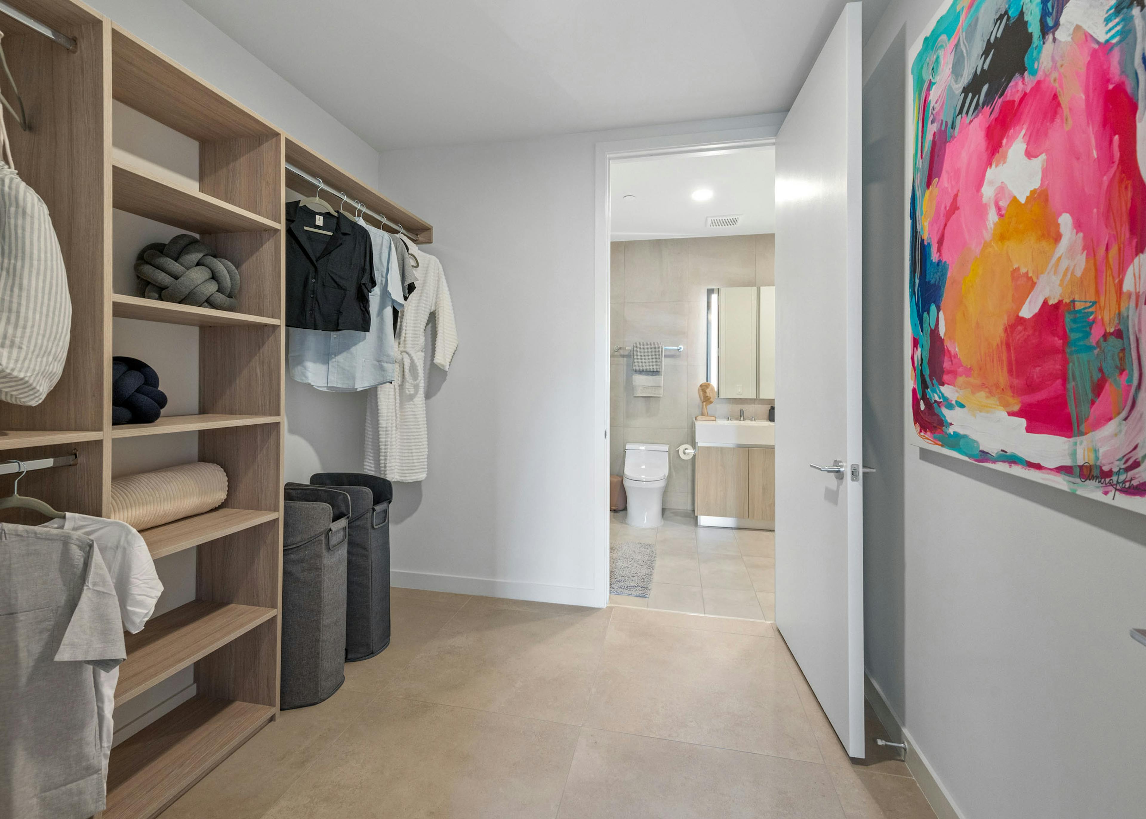 A large walk in closet at AMLI Wynwood apartments leading to a modern bathroom with wooden shelving showing clothing and laundry hampers