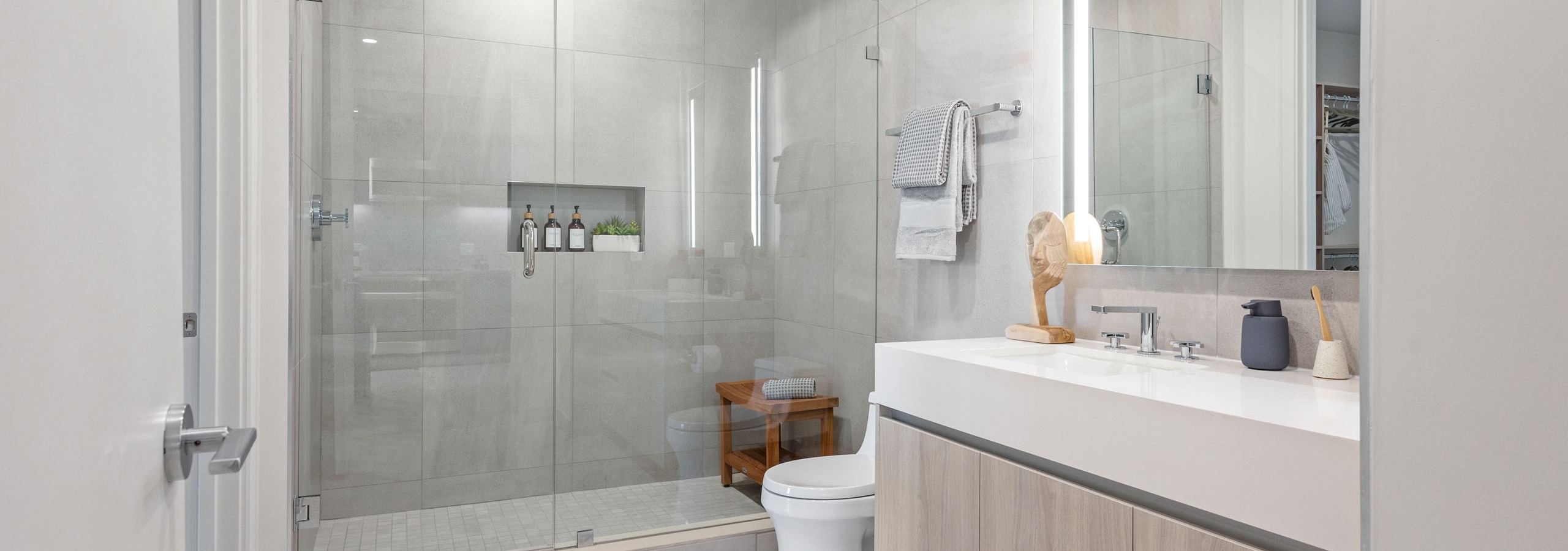 A modern bathroom at AMLI Wynwood apartments with a glass shower and overhead rainfall shower head next to a large sink area