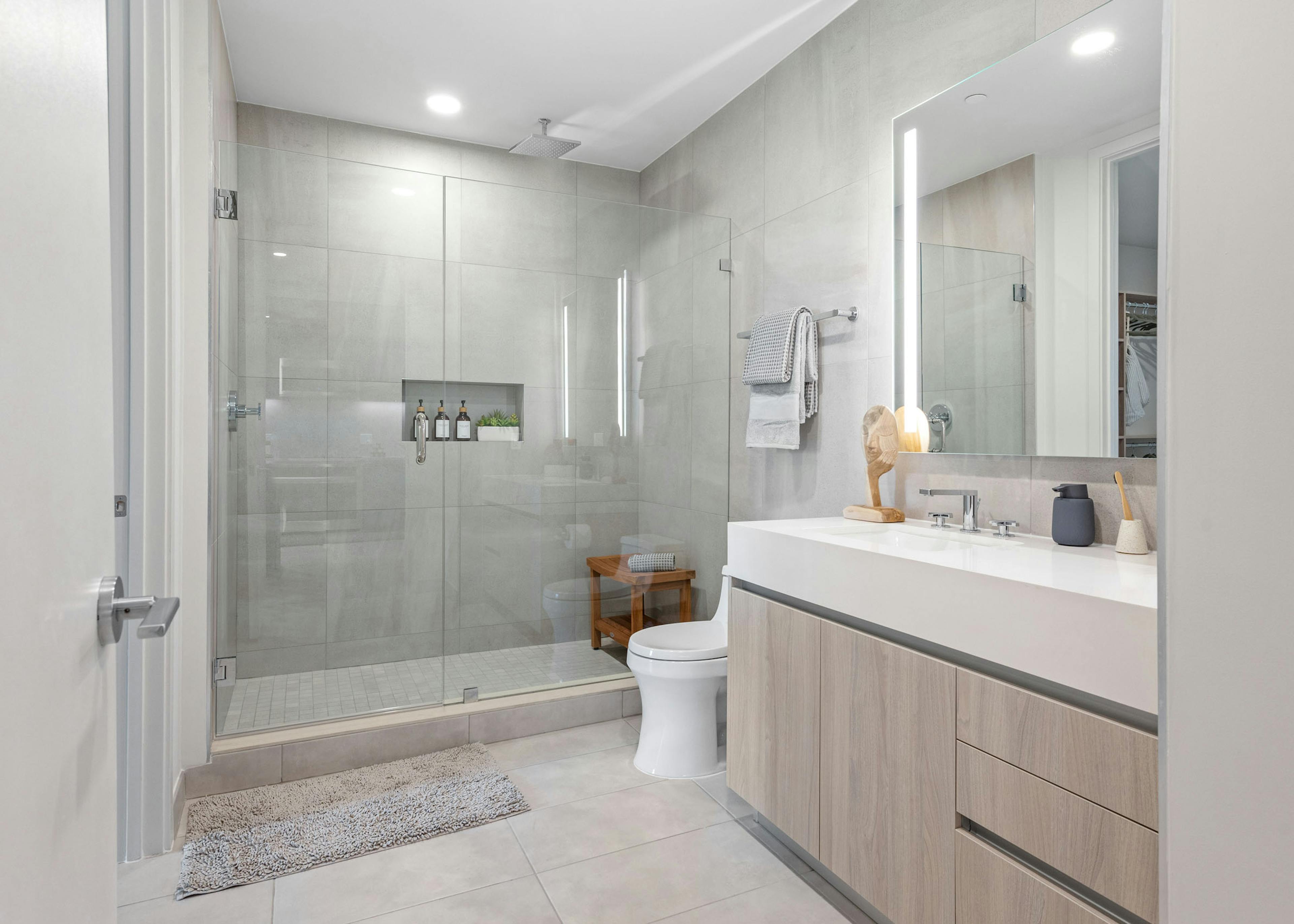 A modern bathroom at AMLI Wynwood apartments with a glass shower and overhead rainfall shower head next to a large sink area