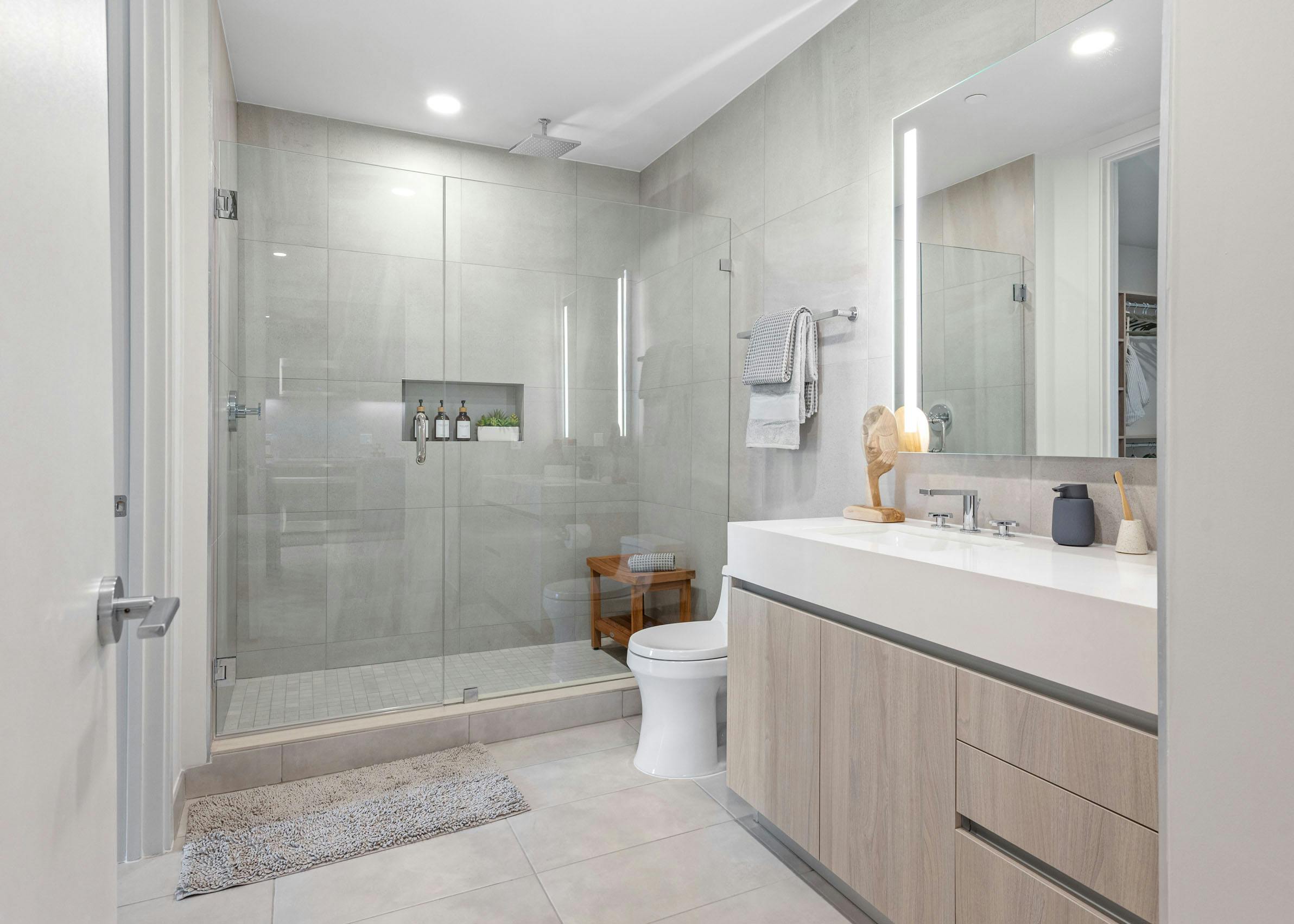 A modern bathroom at AMLI Wynwood apartments with a glass shower and overhead rainfall shower head next to a large sink area