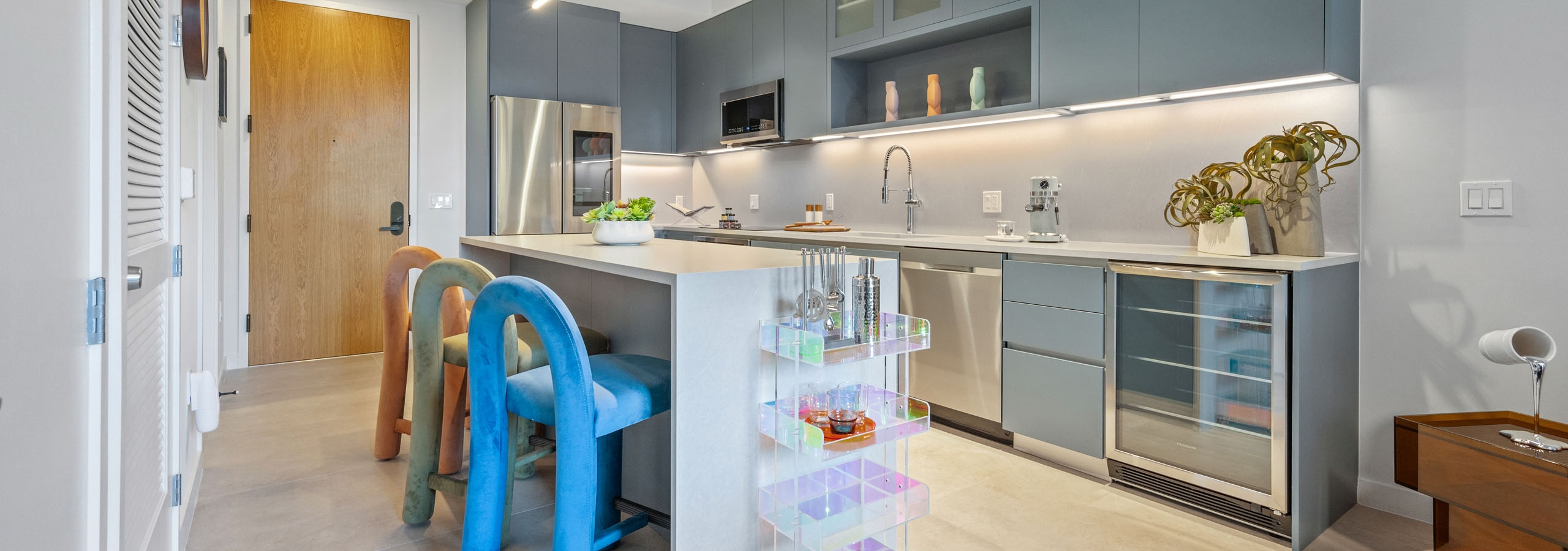 View of a kitchen at AMLI Wynwood apartments showing modern blue cabinets and stainless steel appliances with colorful counter chairs