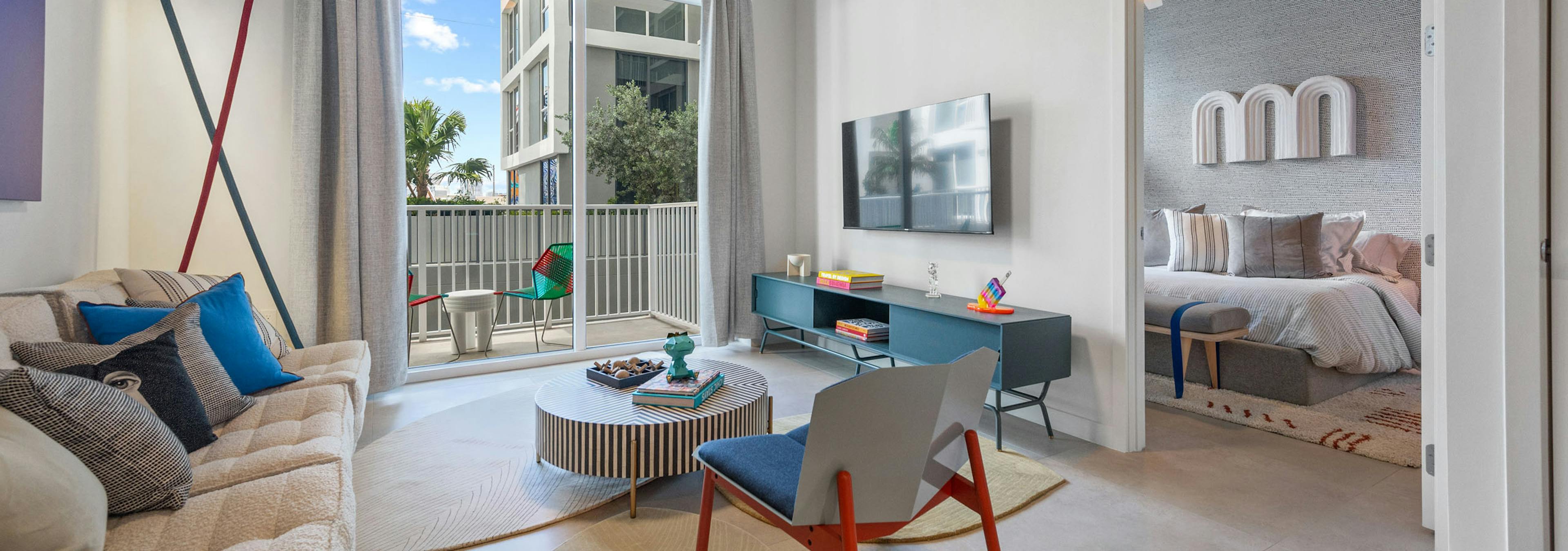 Living room at AMLI Wynwood apartments with whimsical designer furniture and views of a balcony with seating and bedroom with artwork